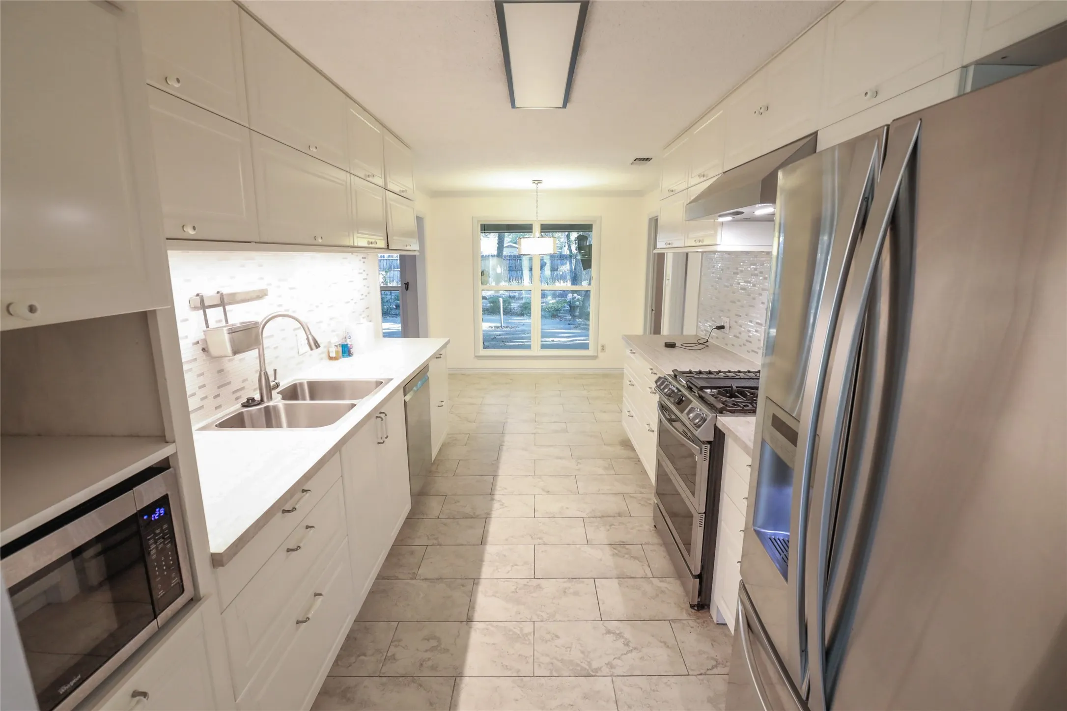 Galley kitchen featuring white cabinetry, light-toned countertops, stainless steel appliances, a tiled backsplash, and tile flooring