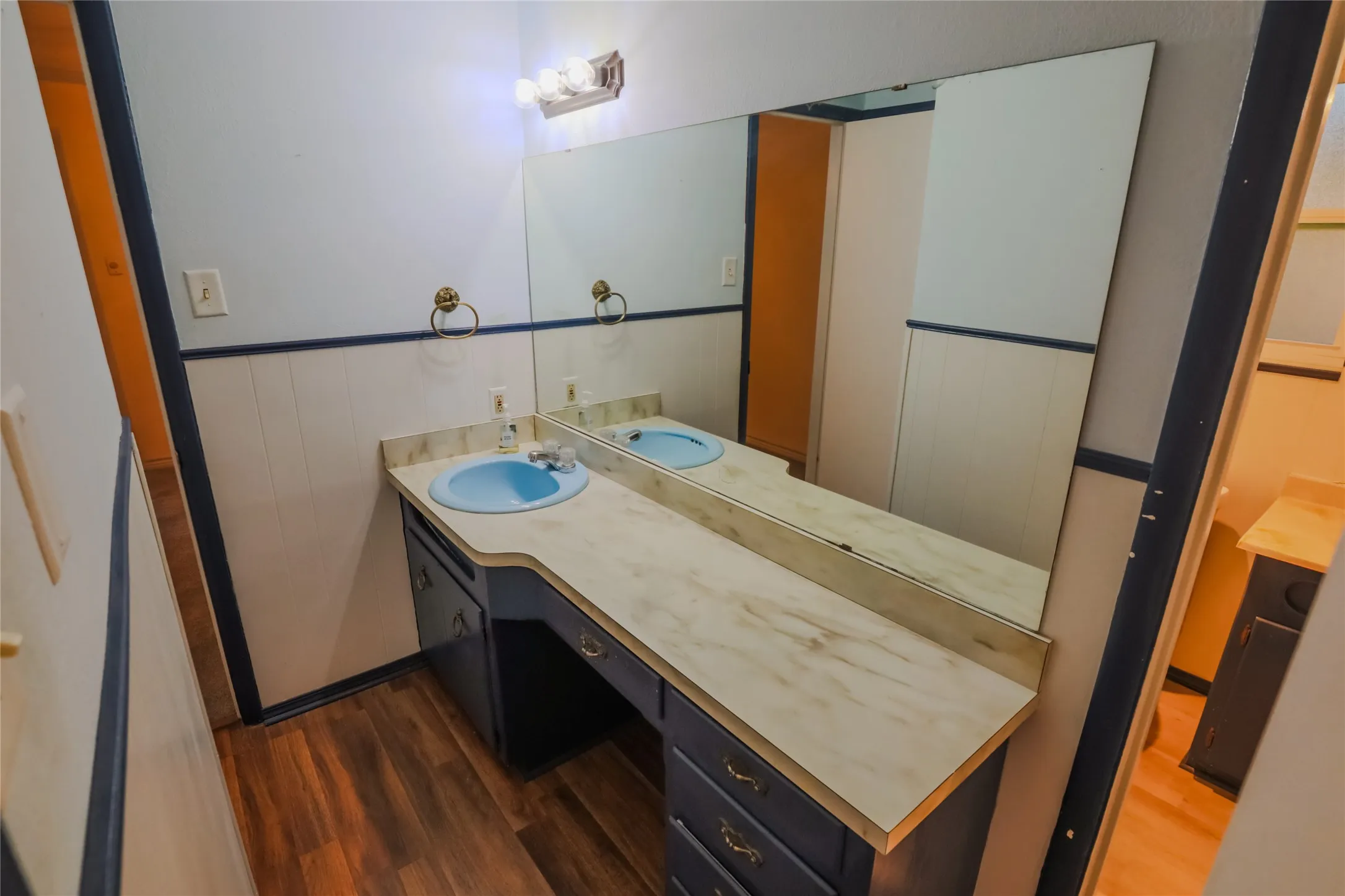 Vanity with an integrated sink, expansive mirror, wood-finish flooring, and wall-mounted lighting