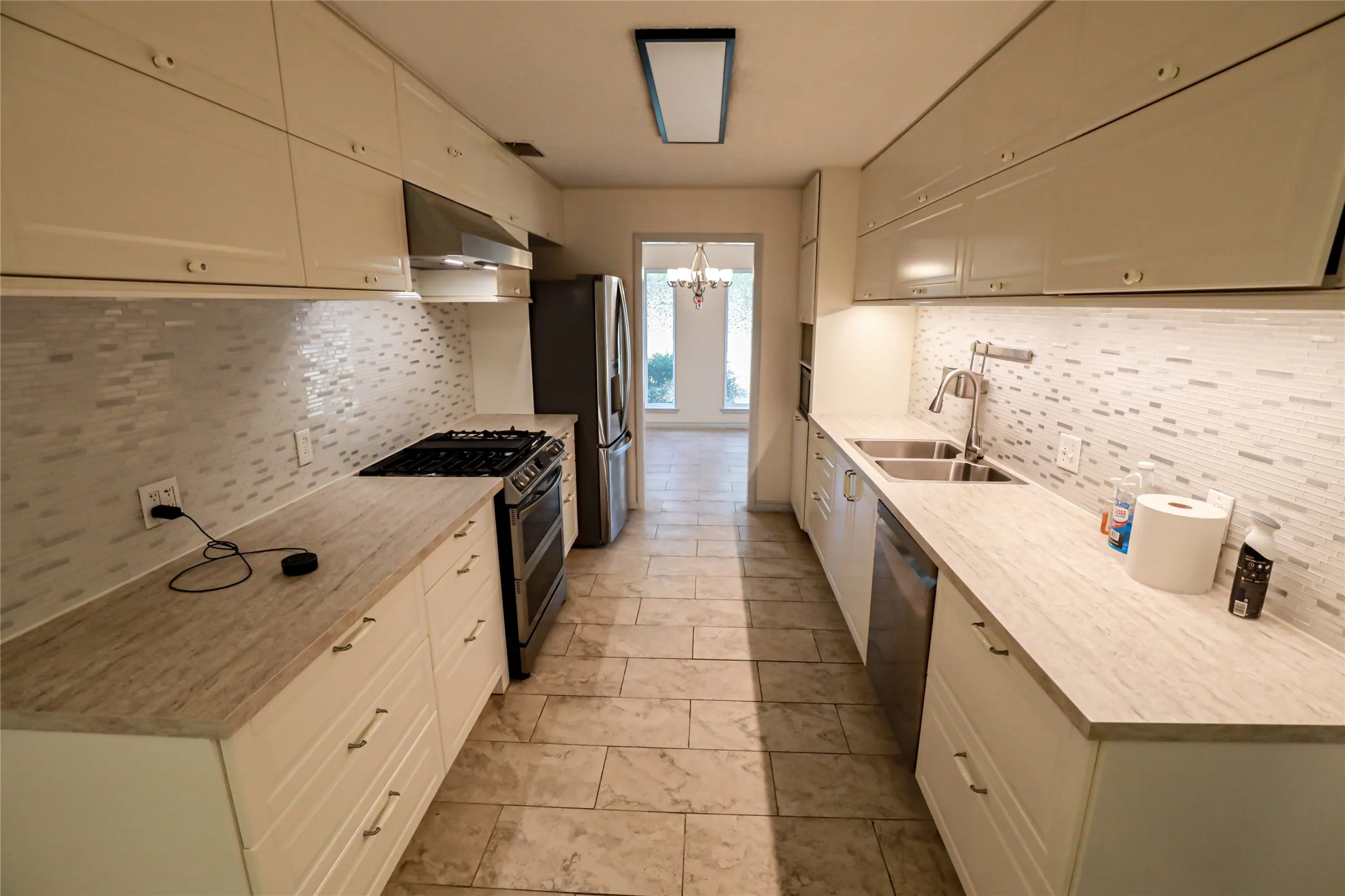 Galley kitchen featuring white cabinetry, stone-look countertops, stainless steel appliances, and a mosaic tile backsplash