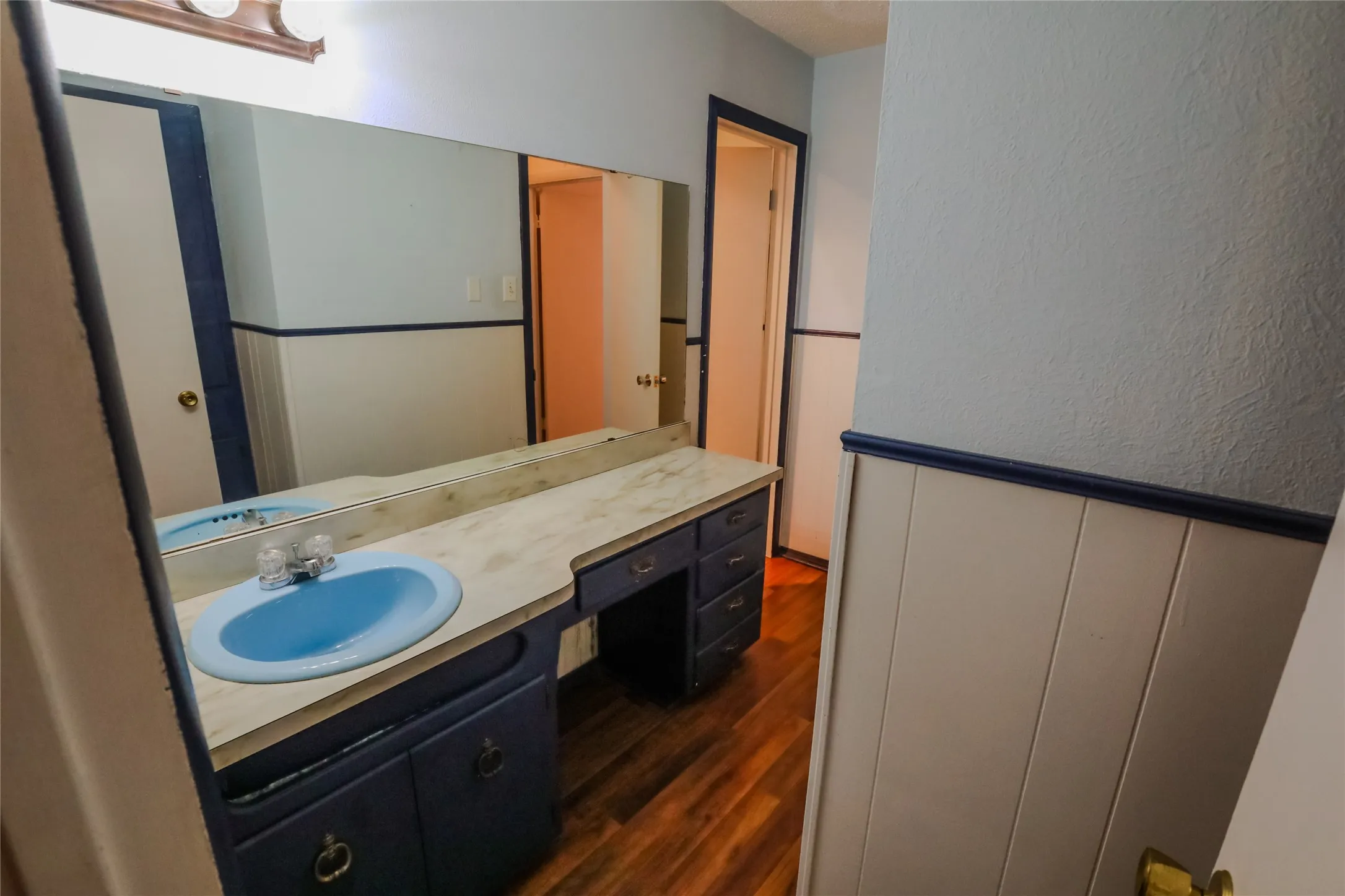 Full-width vanity mirror, wood-finish flooring, built-in vanity with cabinetry, and a blue basin sink