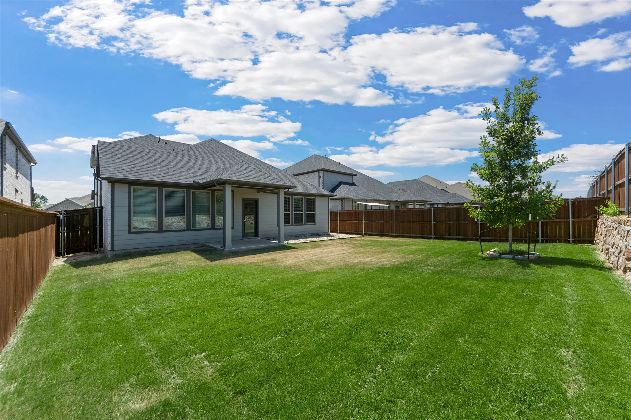 Expansive green lawn with a young tree, concrete patio, and privacy fencing