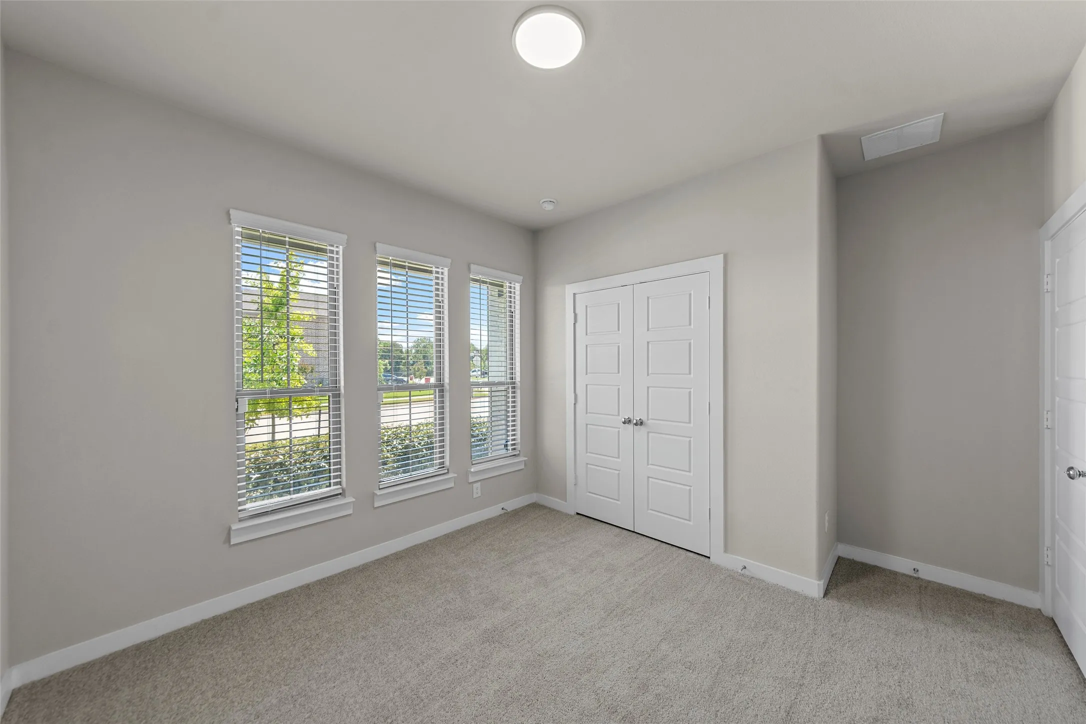 Three windows with blinds, neutral wall paint, carpeted flooring, and white paneled doors