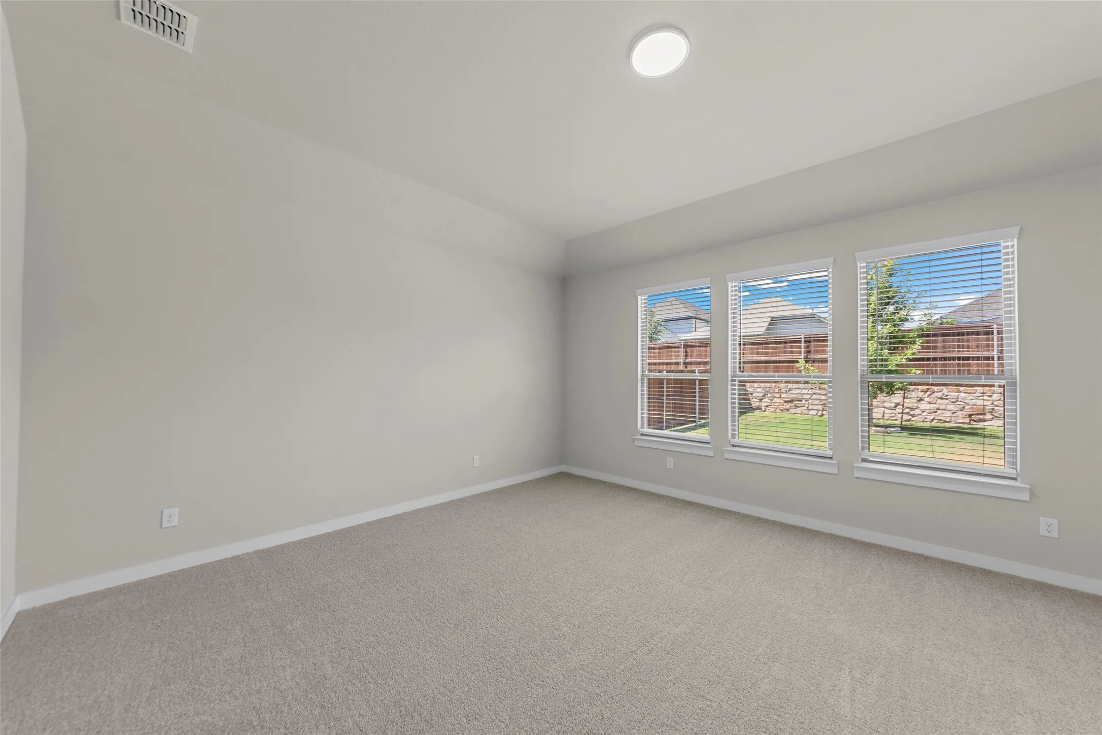 Spacious room featuring carpeting, three large windows with horizontal blinds, and a flush-mount ceiling light
