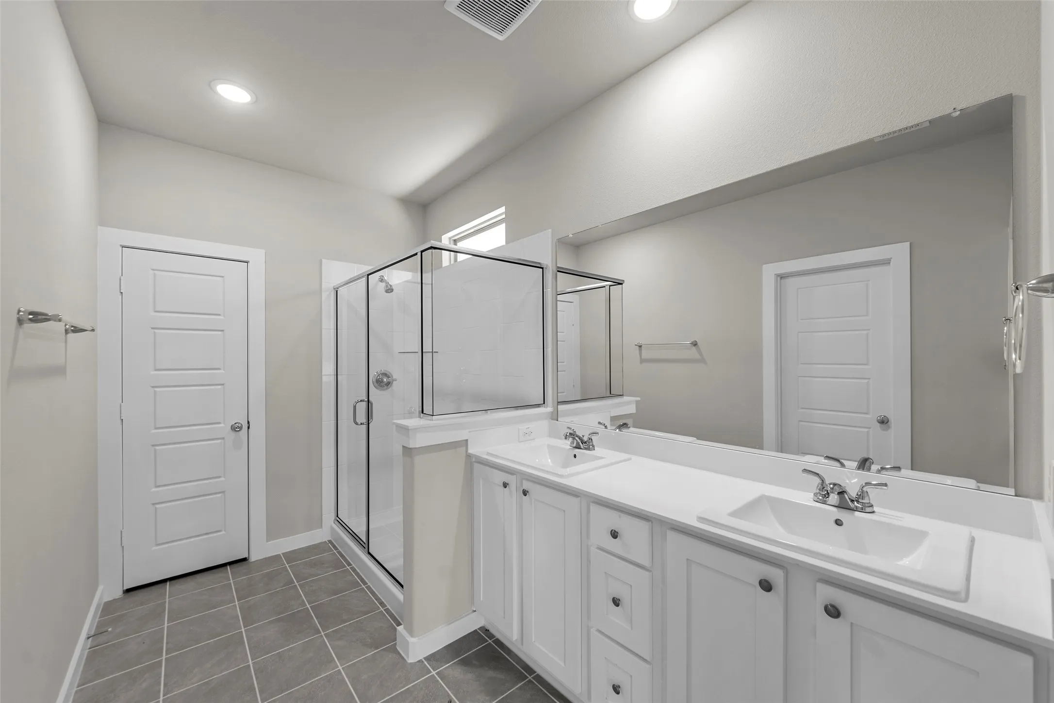 Dual vanity with white cabinetry, tile flooring, glass-enclosed shower, and a large wall mirror