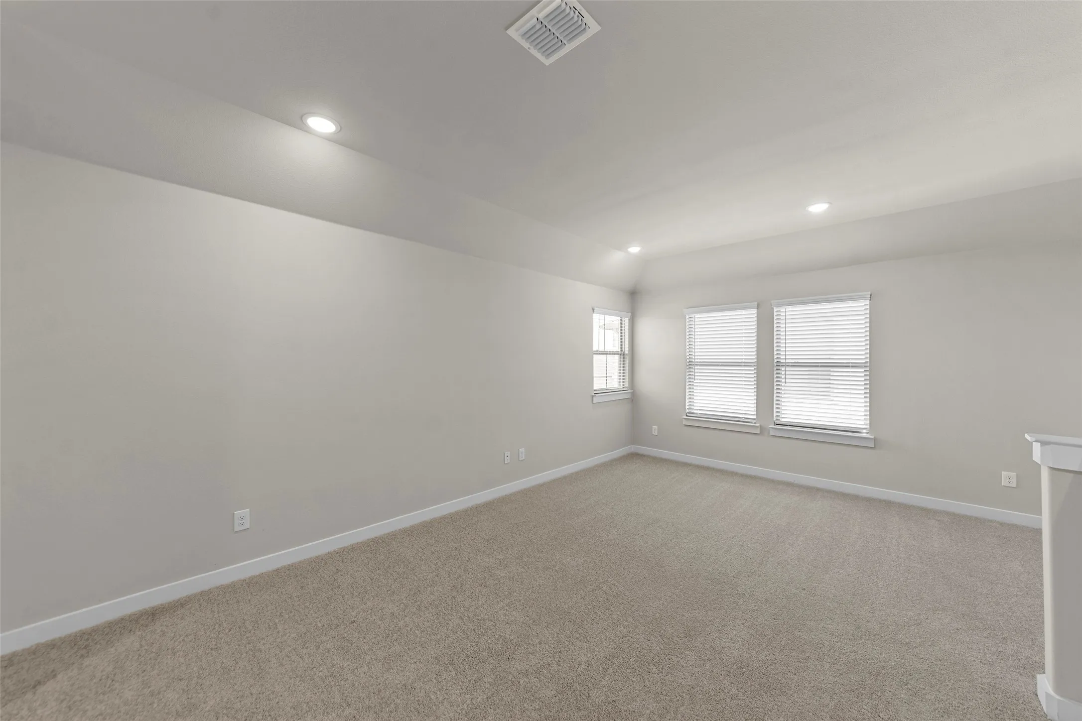 Plush carpeting, recessed lighting, multiple windows with blinds, and neutral wall tones