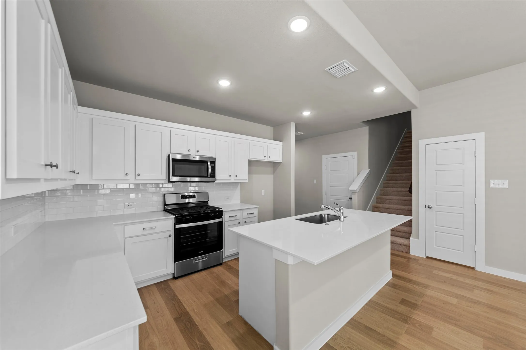 Kitchen featuring white cabinetry, stainless steel appliances, a center island with an undermount sink, white countertops, and wood-finish flooring