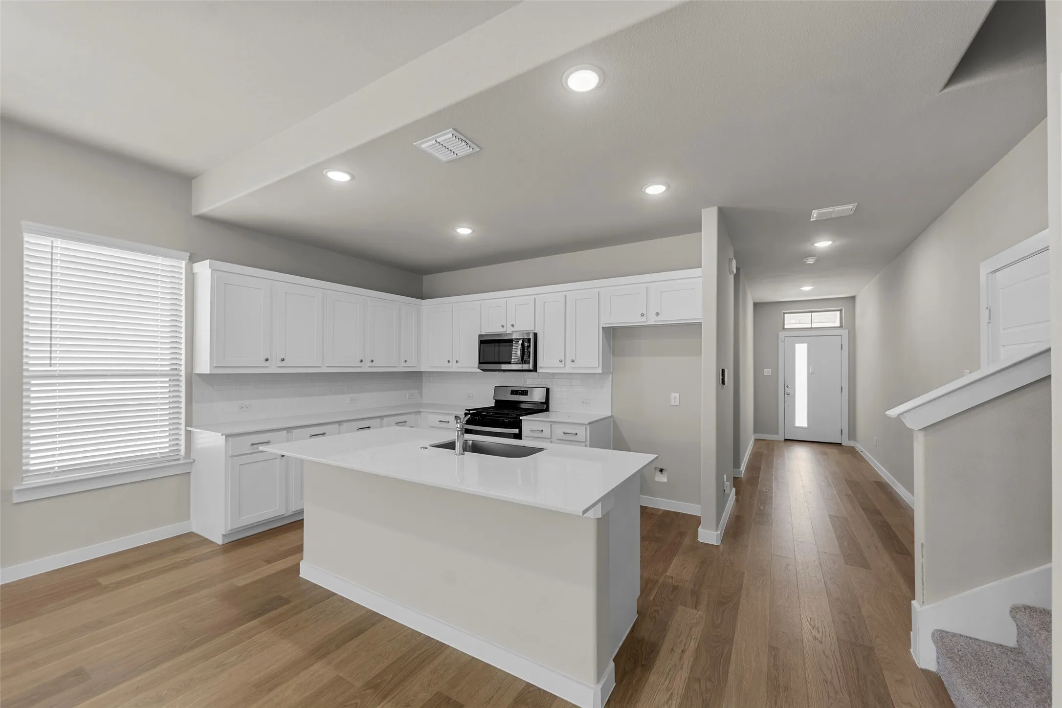 Open-concept living area with wood-finish flooring, recessed lighting, and a kitchen island with an integrated sink