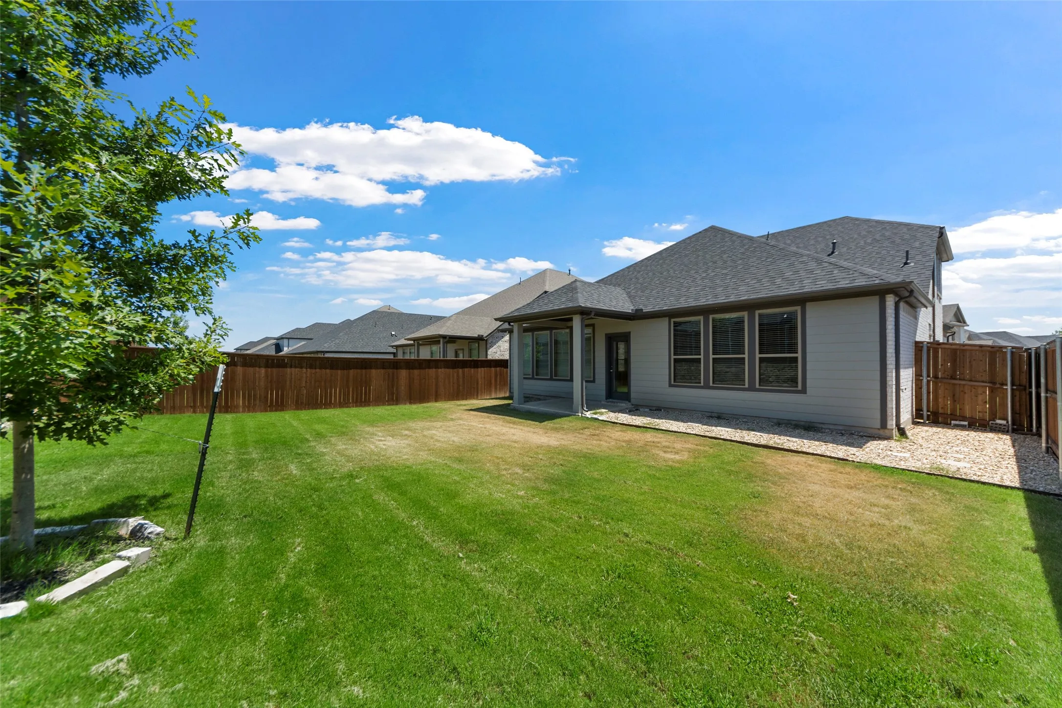 Expansive backyard with a manicured lawn, full privacy fencing, and a covered patio