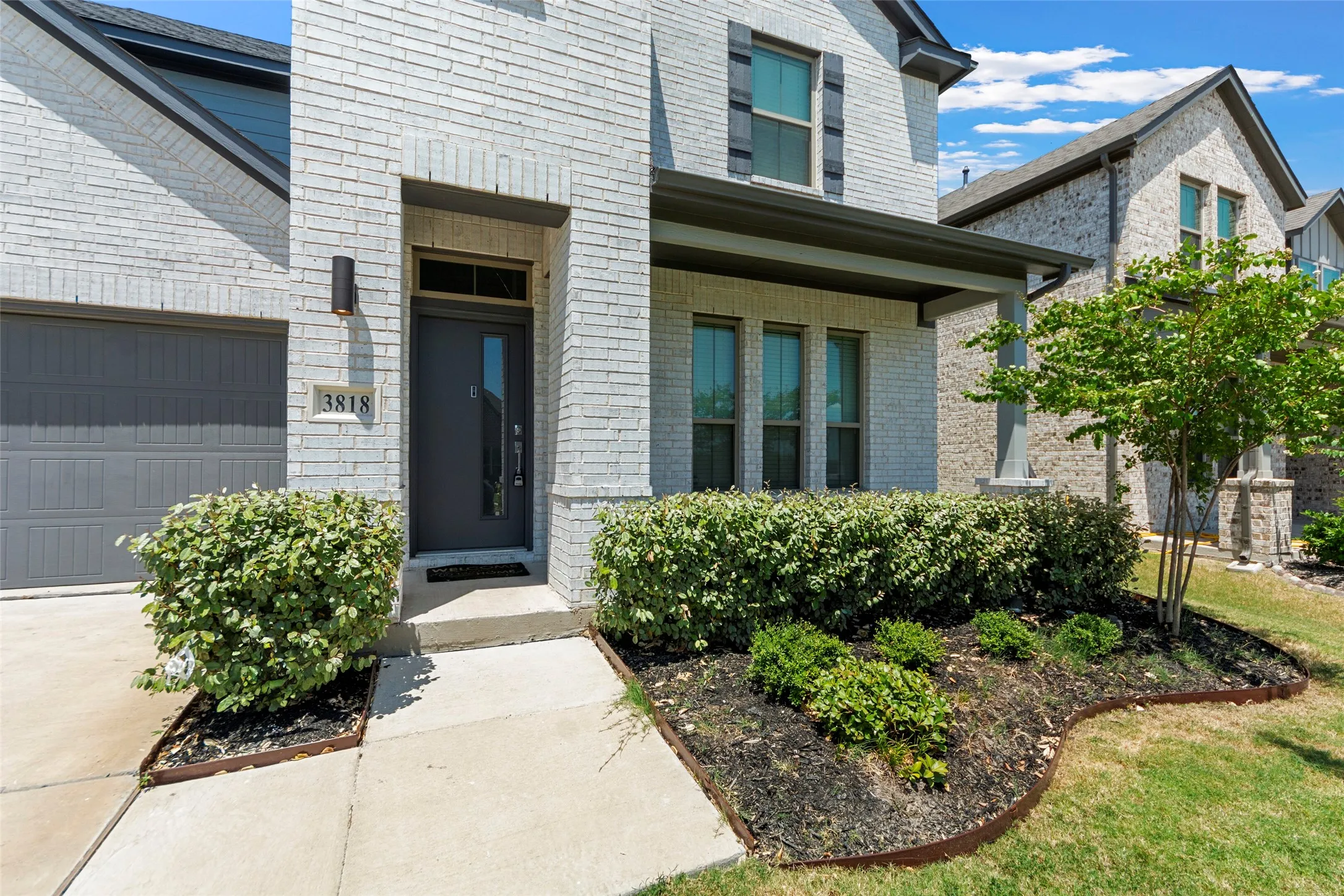 White brick exterior with dark trim accents, covered front porch, and an attached garage