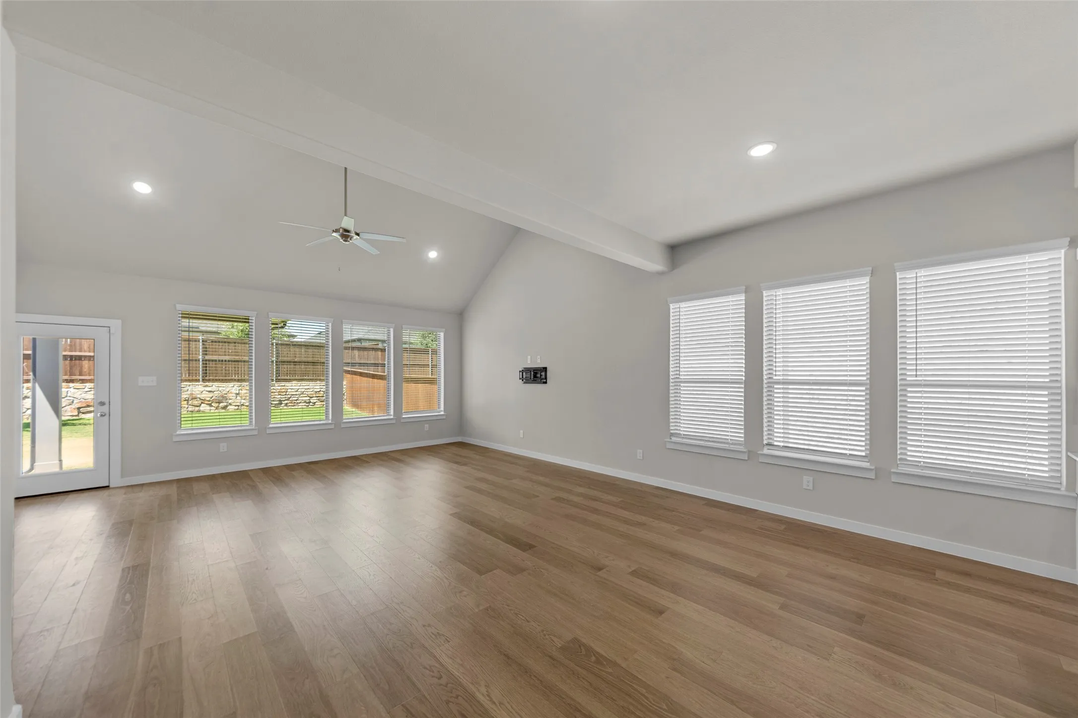 Vaulted ceiling with exposed beam, wood-finish flooring, recessed lighting, ceiling fan, and multiple large windows