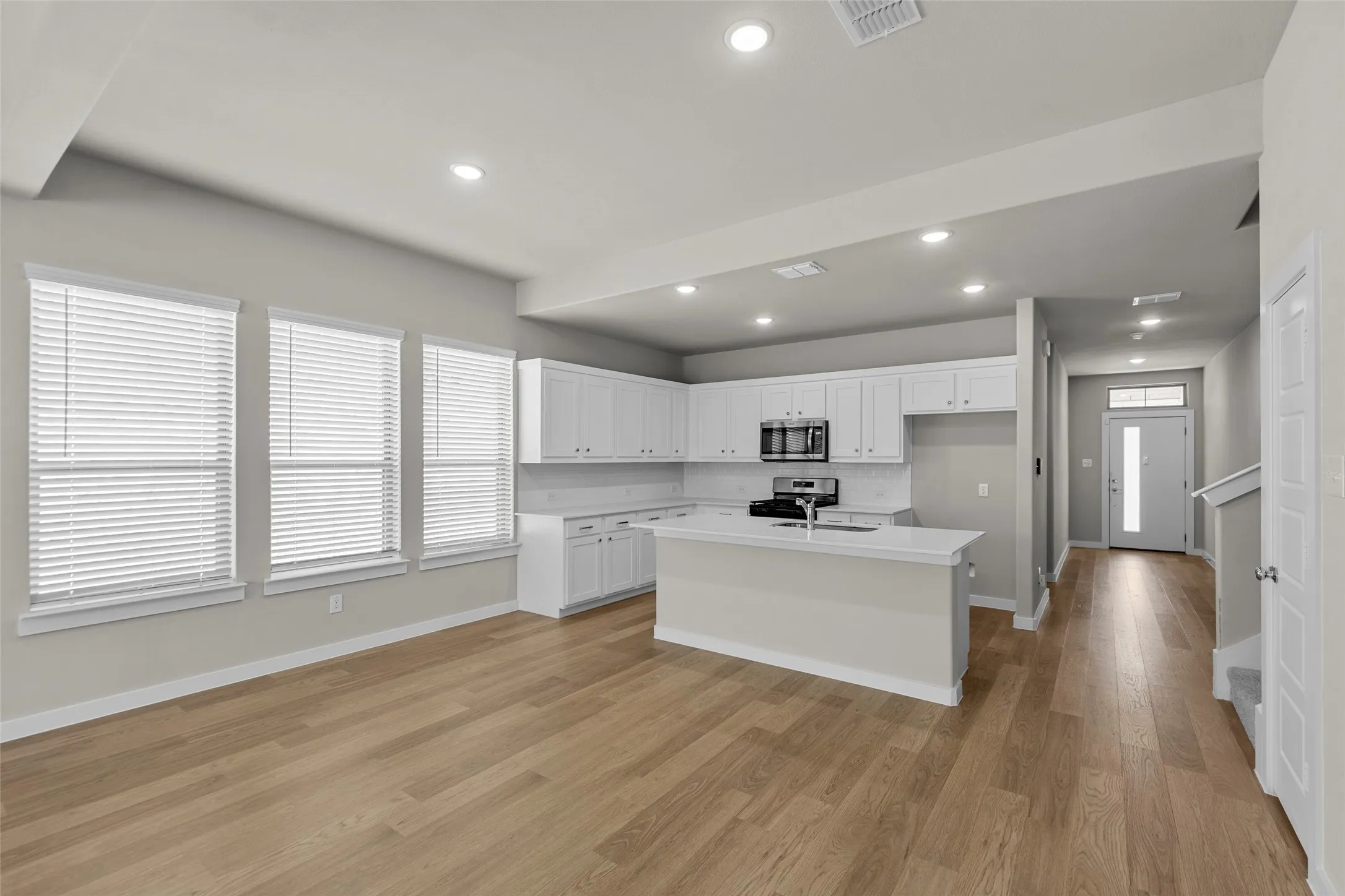 Open-concept living space featuring wood-finish flooring, recessed lighting, and a kitchen with white cabinetry