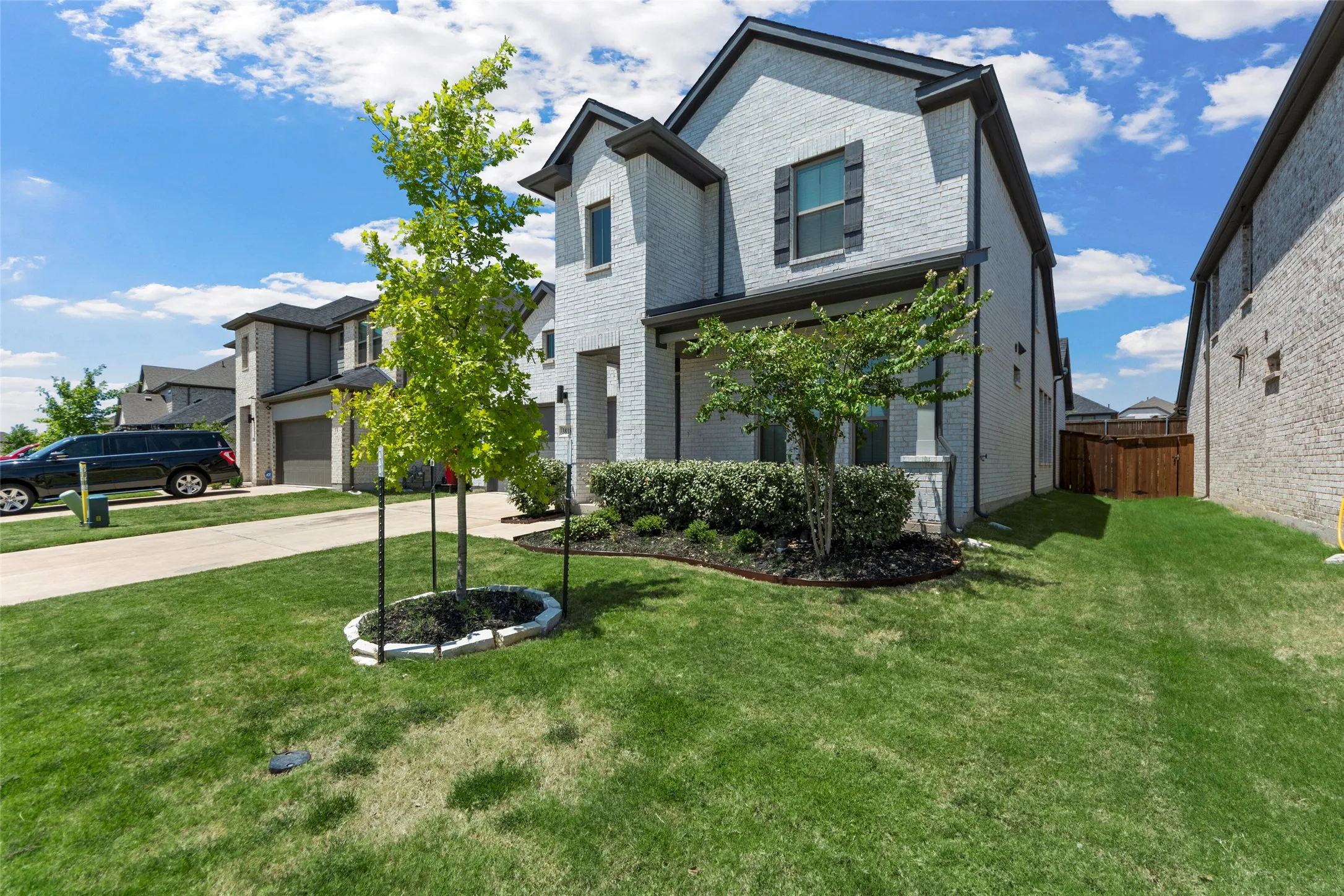 Brick exterior with dark shutters and trim, a manicured lawn, and mature landscaping