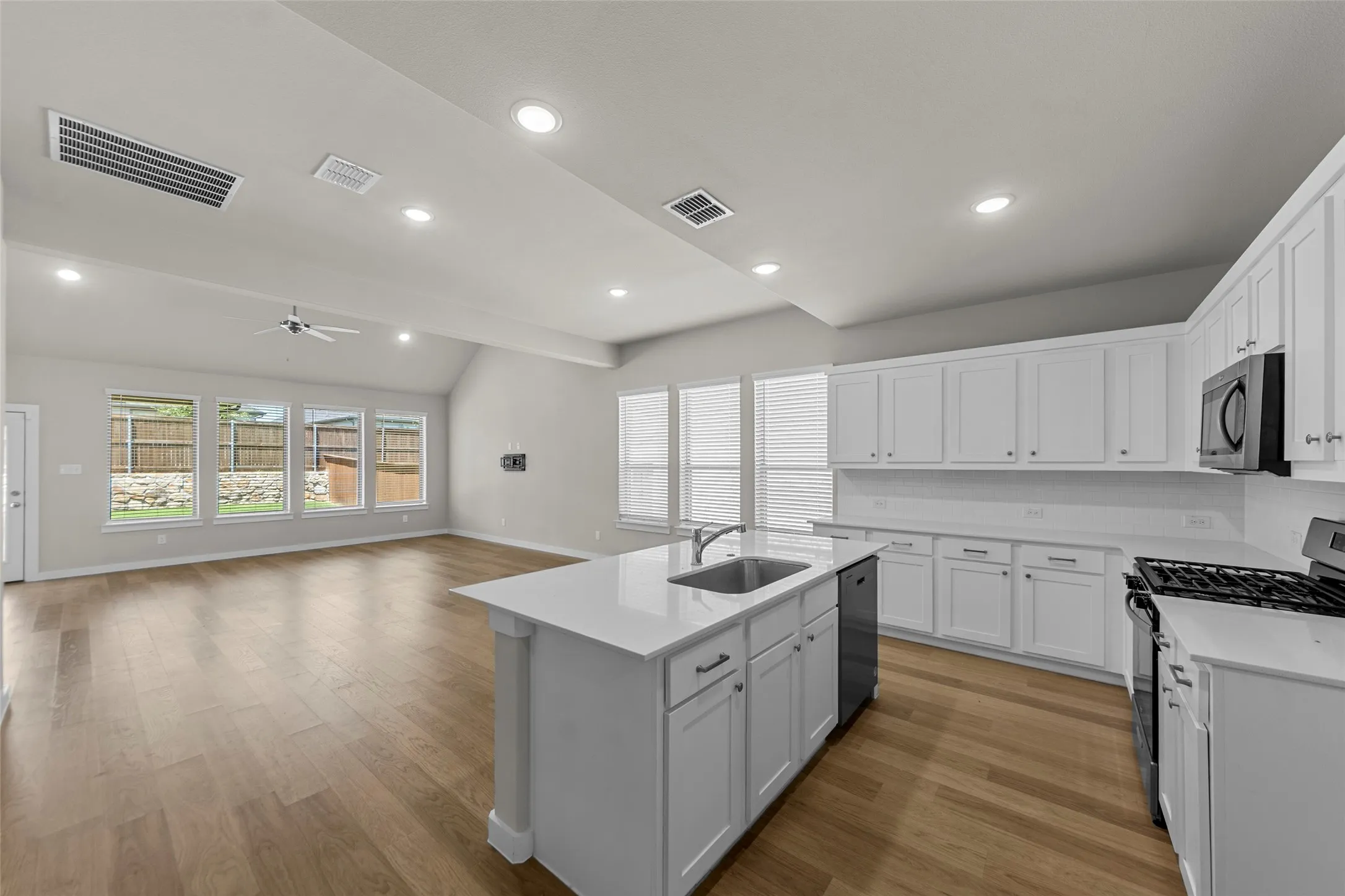 Open-concept kitchen and living area featuring wood-finish flooring, white cabinetry, a kitchen island with an integrated sink, and recessed lighting