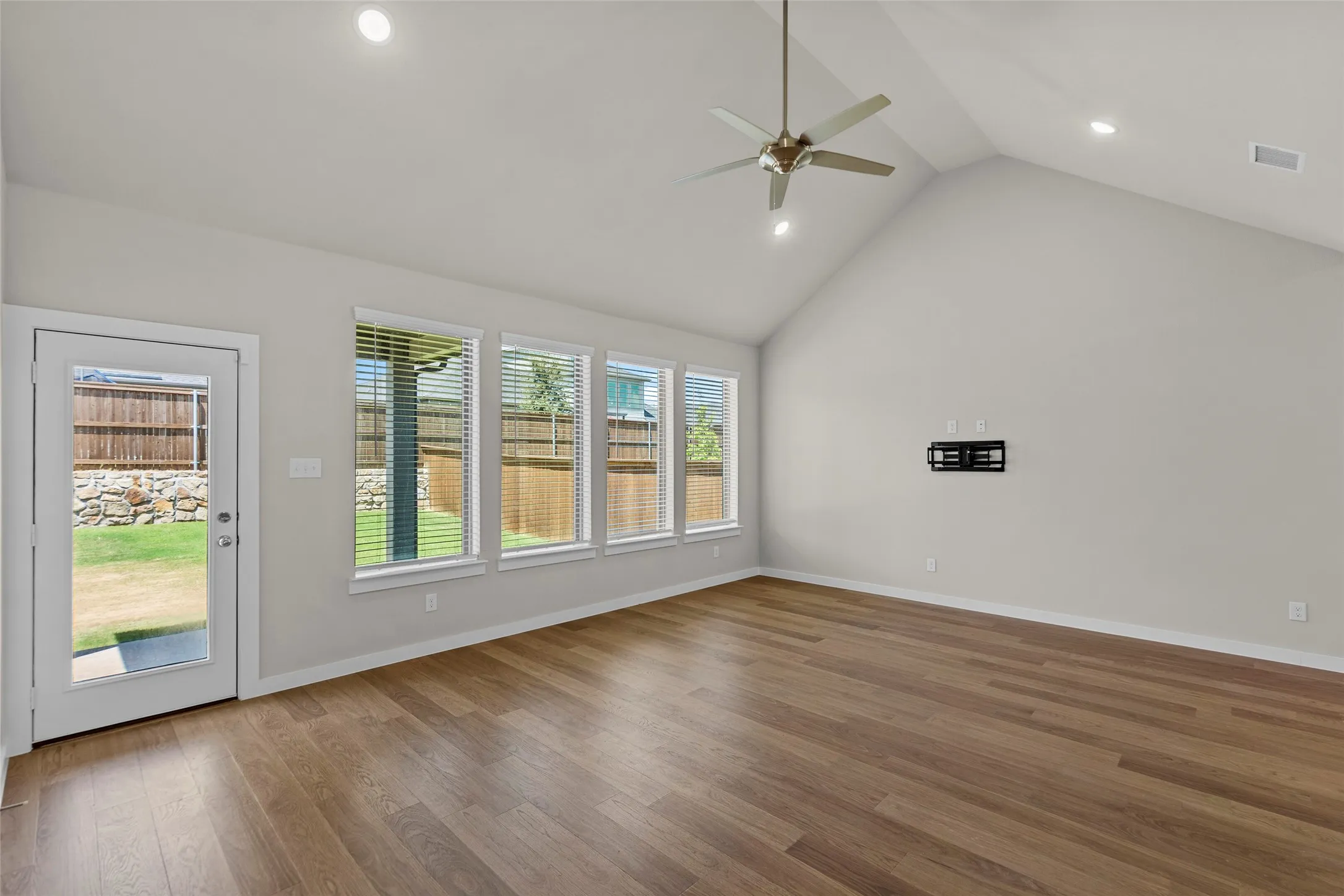 Vaulted ceiling with recessed lighting and a ceiling fan, wood-finish flooring, multiple windows with blinds, and a glass-paneled exterior door