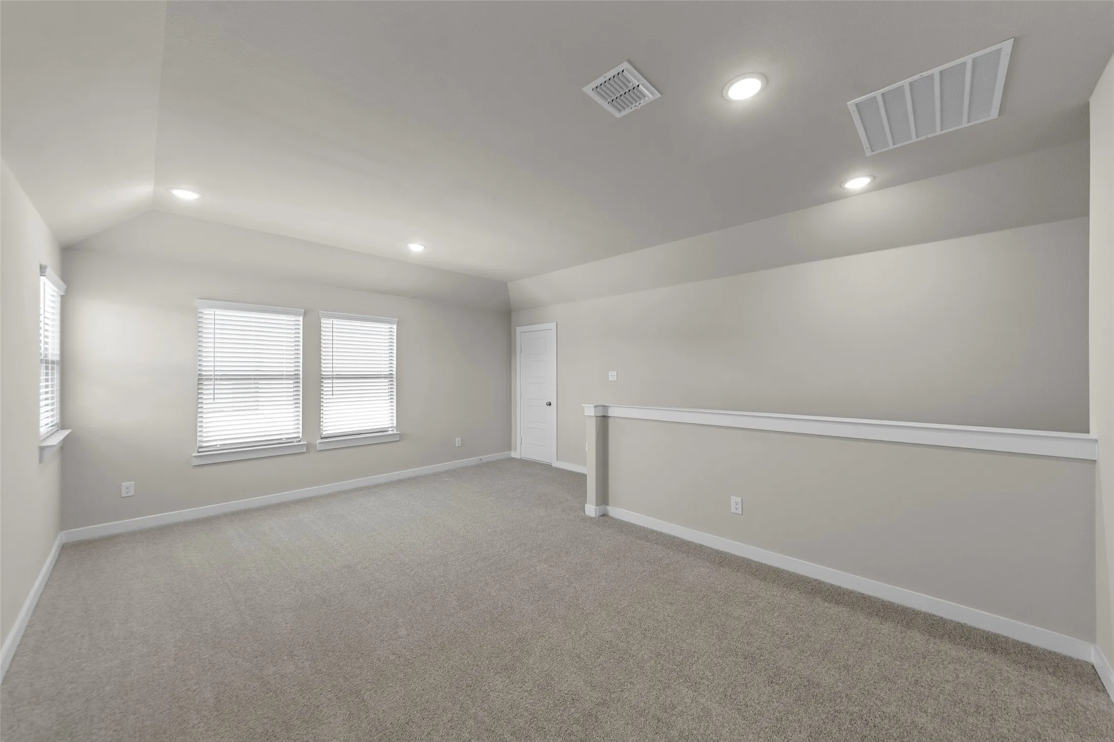 Carpeted room with vaulted ceiling, recessed lighting, double windows, and a built-in half-wall railing