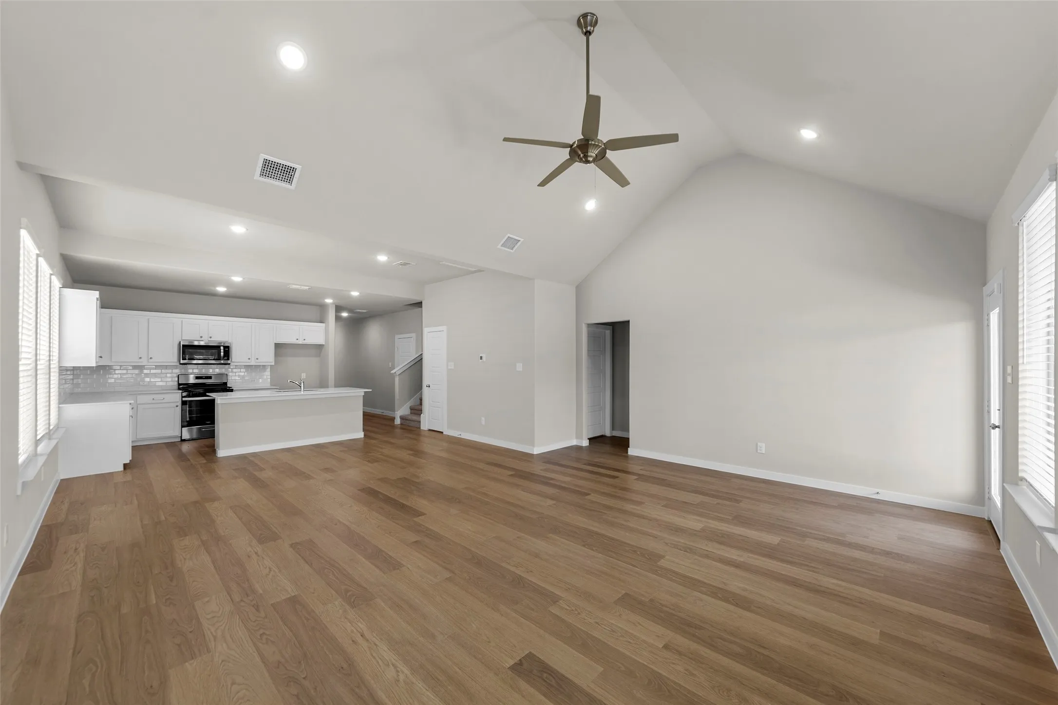 Vaulted ceiling with a ceiling fan, recessed lighting, wood-finish flooring, white kitchen cabinetry, and stainless steel appliances