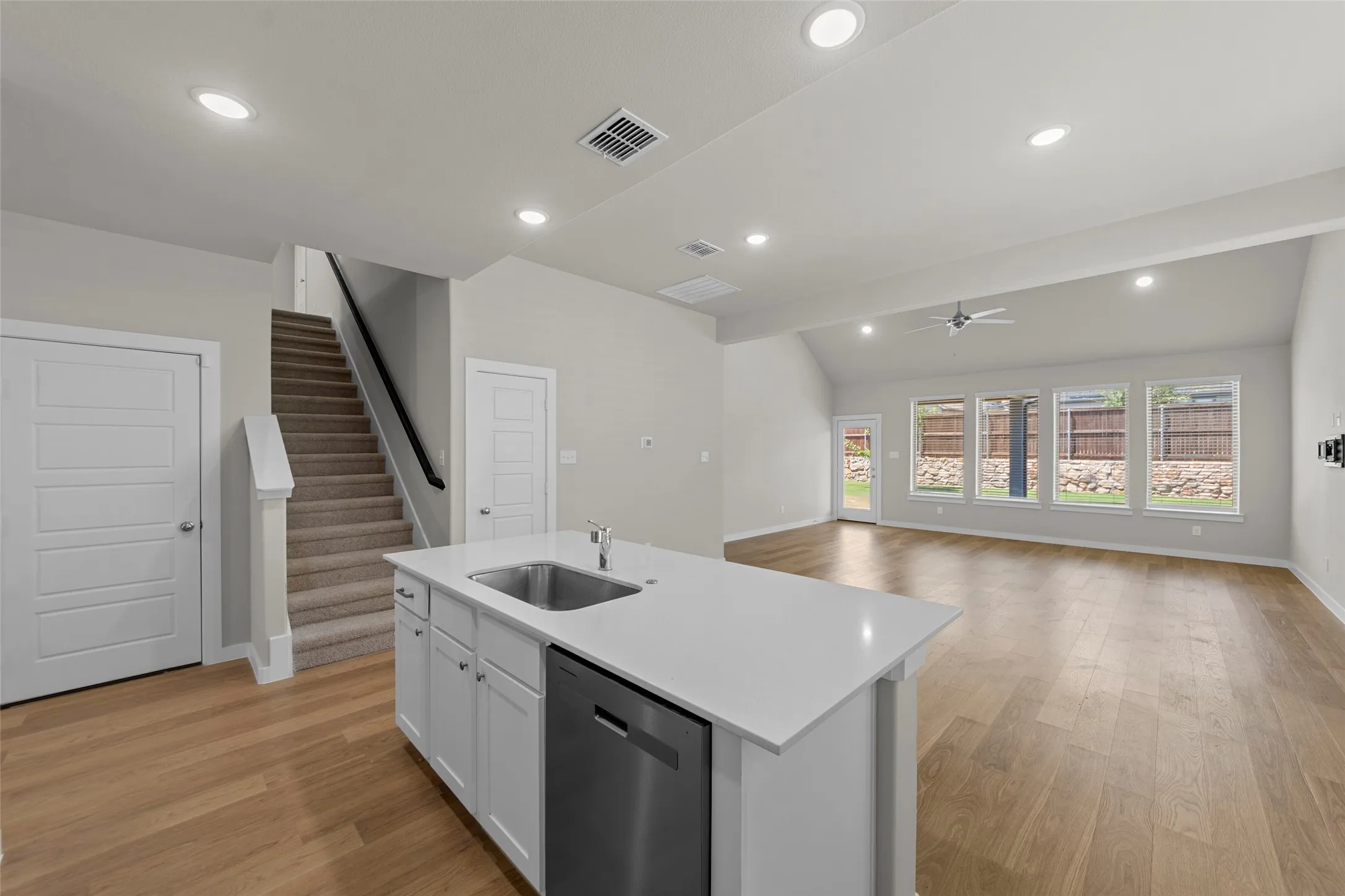 Open-concept living area featuring wood-finish flooring, recessed lighting, a kitchen island with sink, and a vaulted ceiling