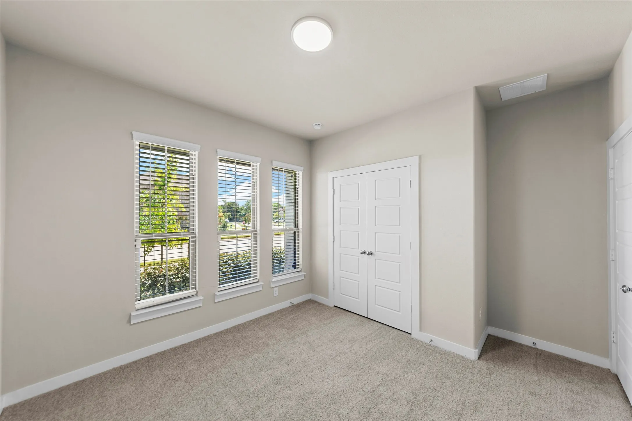 Neutral wall color, carpet flooring, three tall windows with blinds, recessed lighting, and a paneled double door