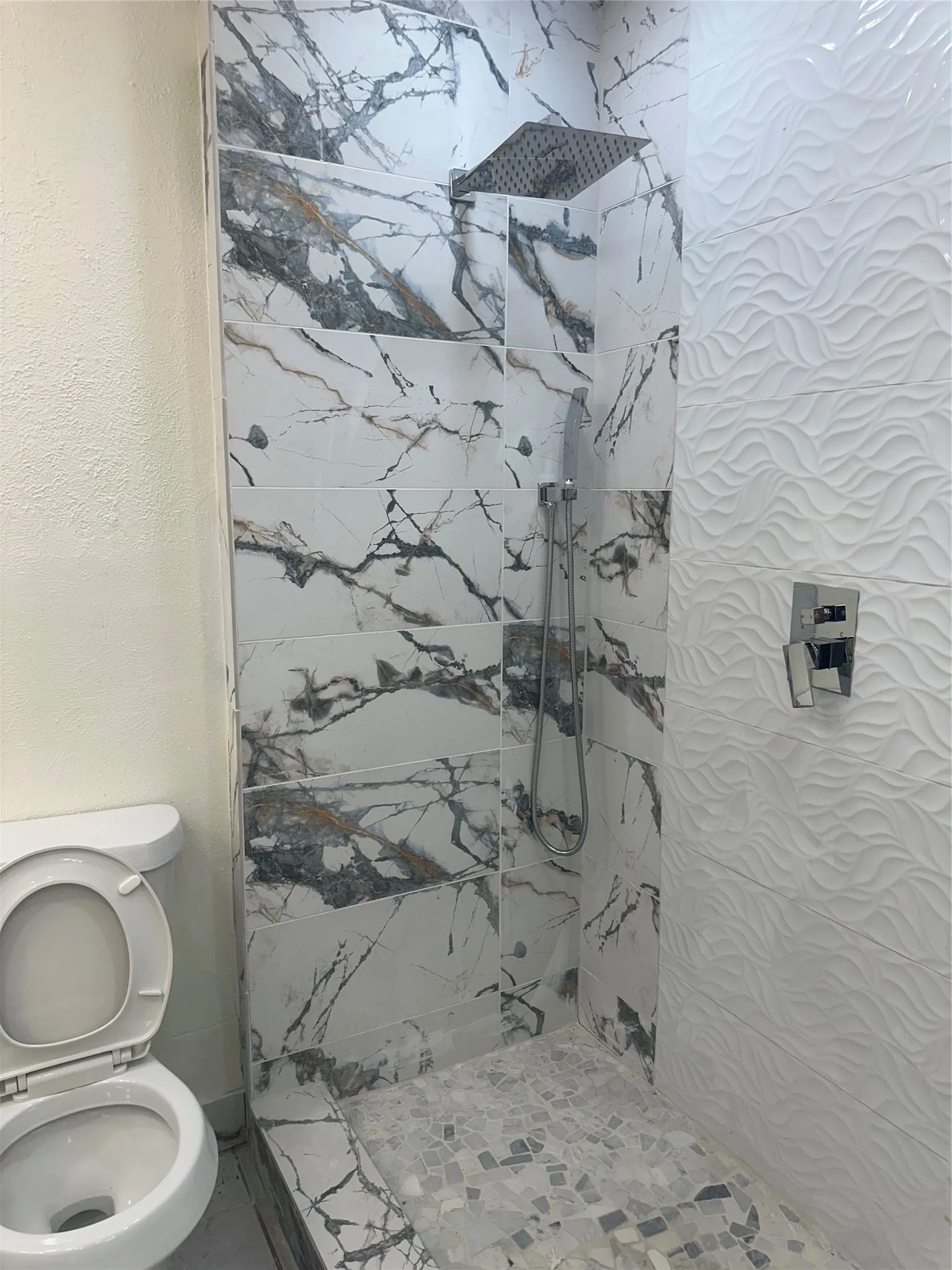 Walk-in shower with large-format marbled tile, mosaic floor tile, and a rain showerhead