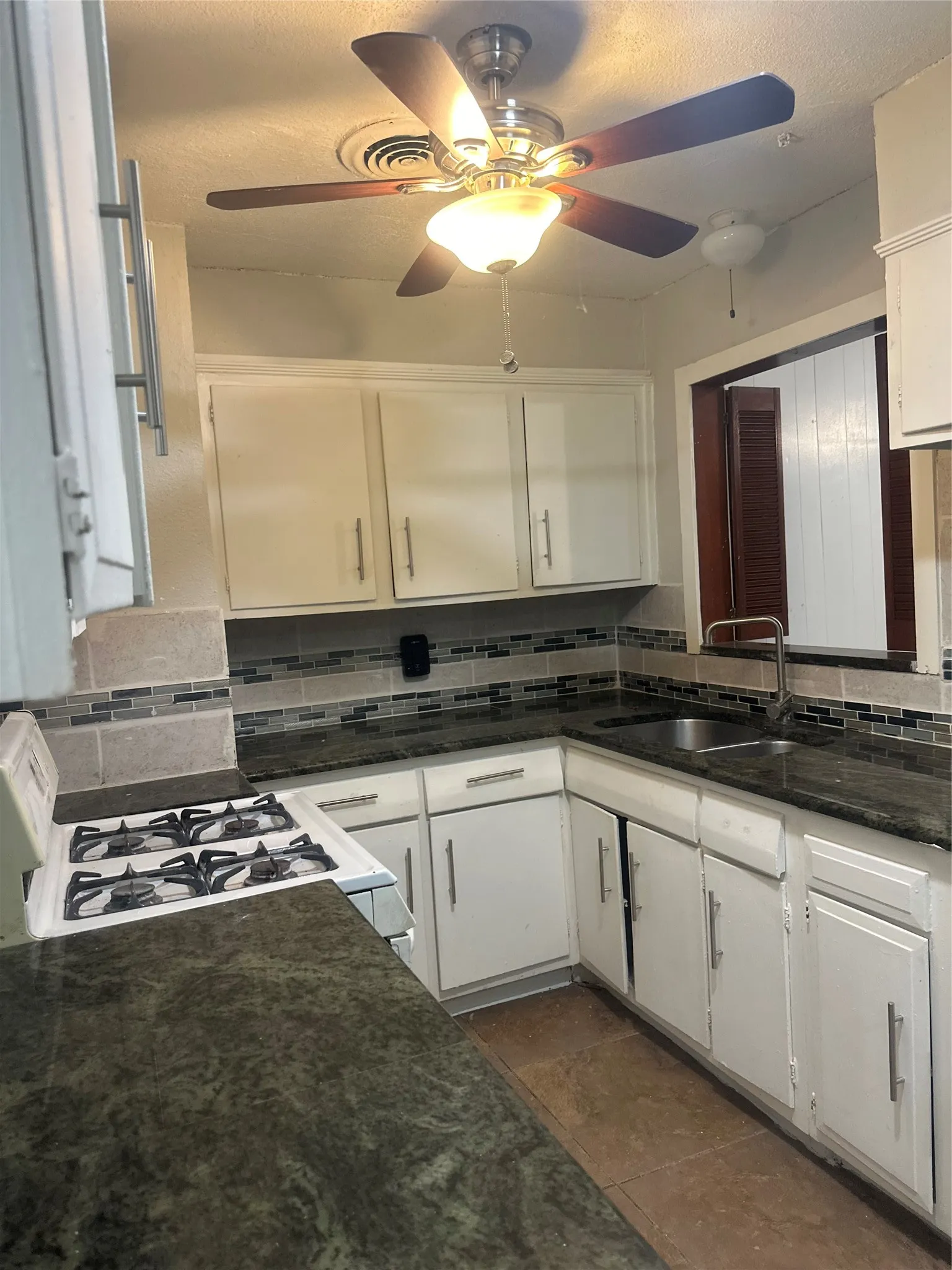 U-shaped kitchen featuring white cabinetry with silver-tone hardware, dark countertops, a gas range, and a ceiling fan with integrated lighting