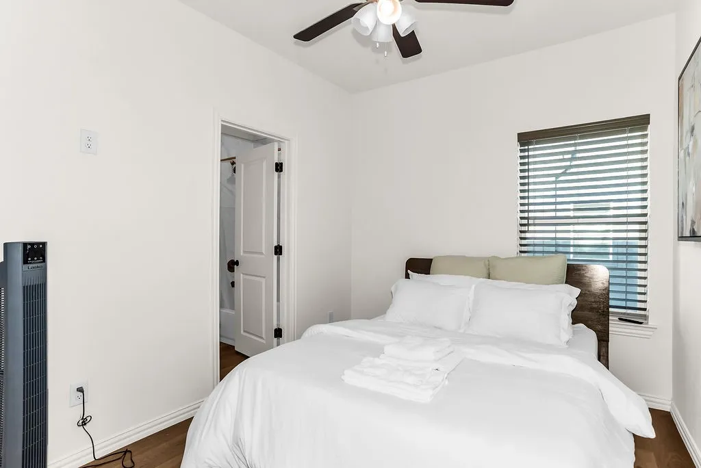 Wood-finish flooring with white baseboards, a ceiling fan with light fixture, and a window with horizontal blinds