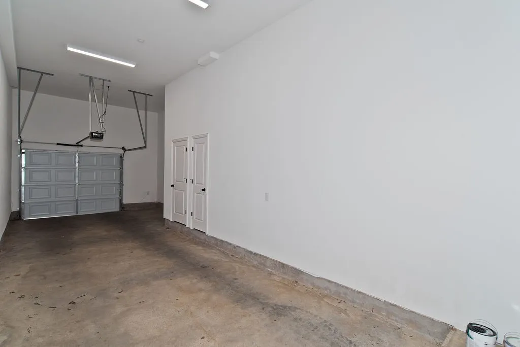 Concrete flooring, dual white bi-fold doors, overhead garage door with opener, and linear fluorescent lighting
