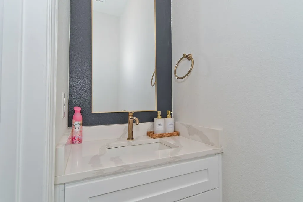 White vanity with shaker-style cabinetry, an integrated rectangular sink, and a gold-finish single-handle faucet