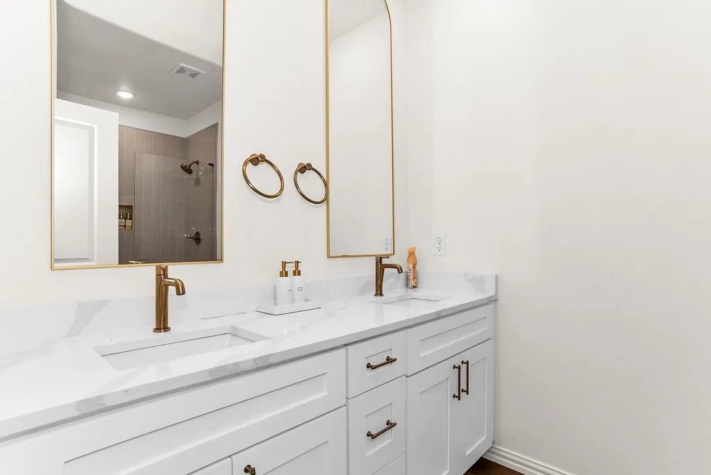 Dual undermount sinks with brushed gold fixtures, white shaker cabinetry, and a light-toned countertop