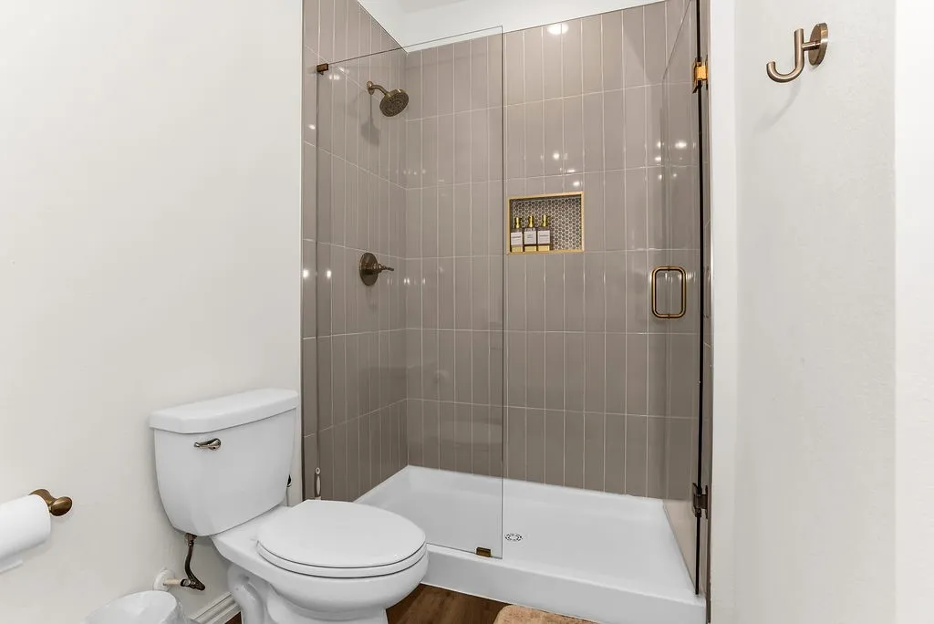 Modern bathroom featuring a frameless glass-enclosed shower with vertical tile surround, white subway tile walls, and brushed bronze hardware