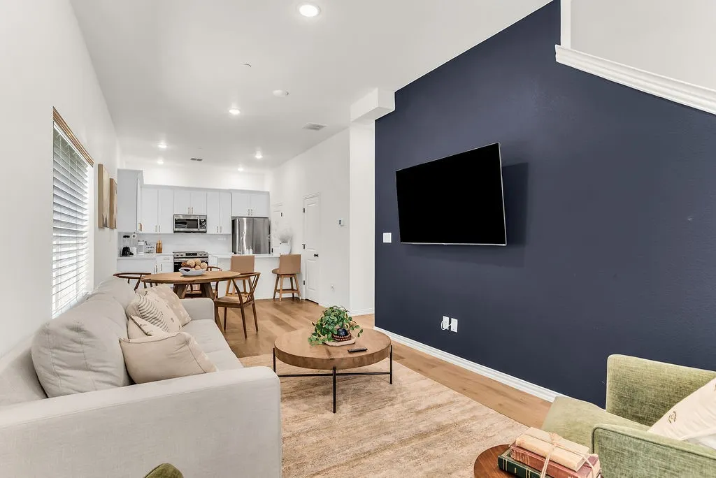 Open-concept living space with wood-finish flooring, recessed lighting, and a kitchen featuring white cabinetry, stainless steel appliances, and a tiled backsplash