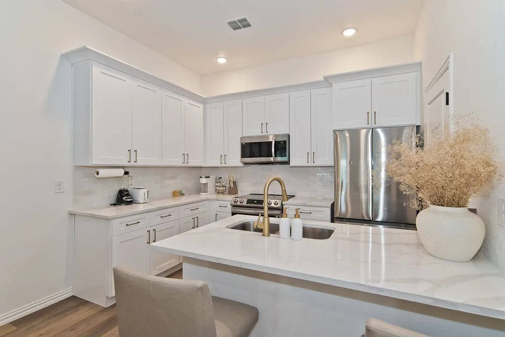 Contemporary kitchen featuring white shaker-style cabinetry with brushed nickel hardware, quartz countertops, and a waterfall-edge island