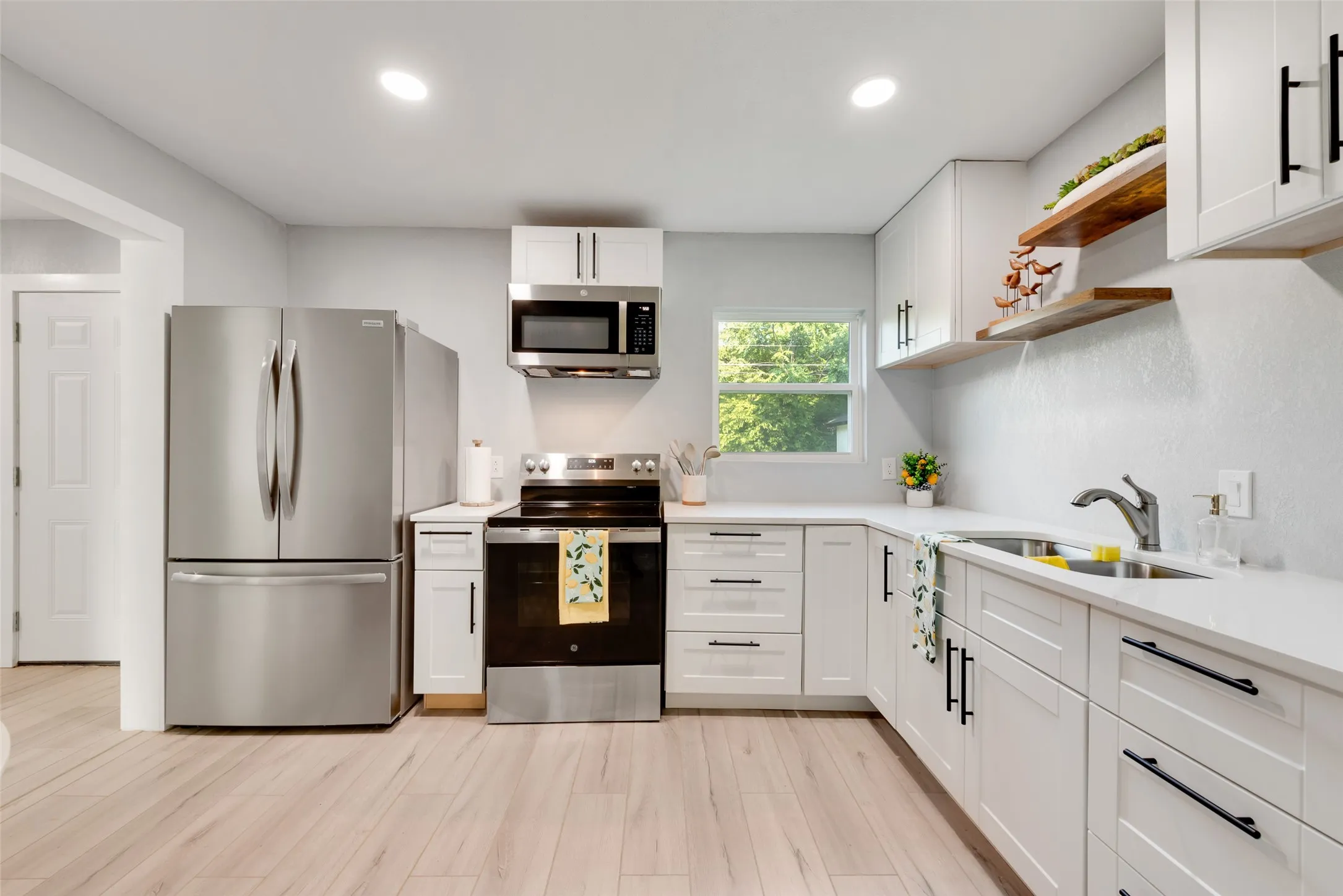 White cabinetry with black hardware, stainless steel appliances, light wood-finish flooring, and a stainless steel sink with a gooseneck faucet