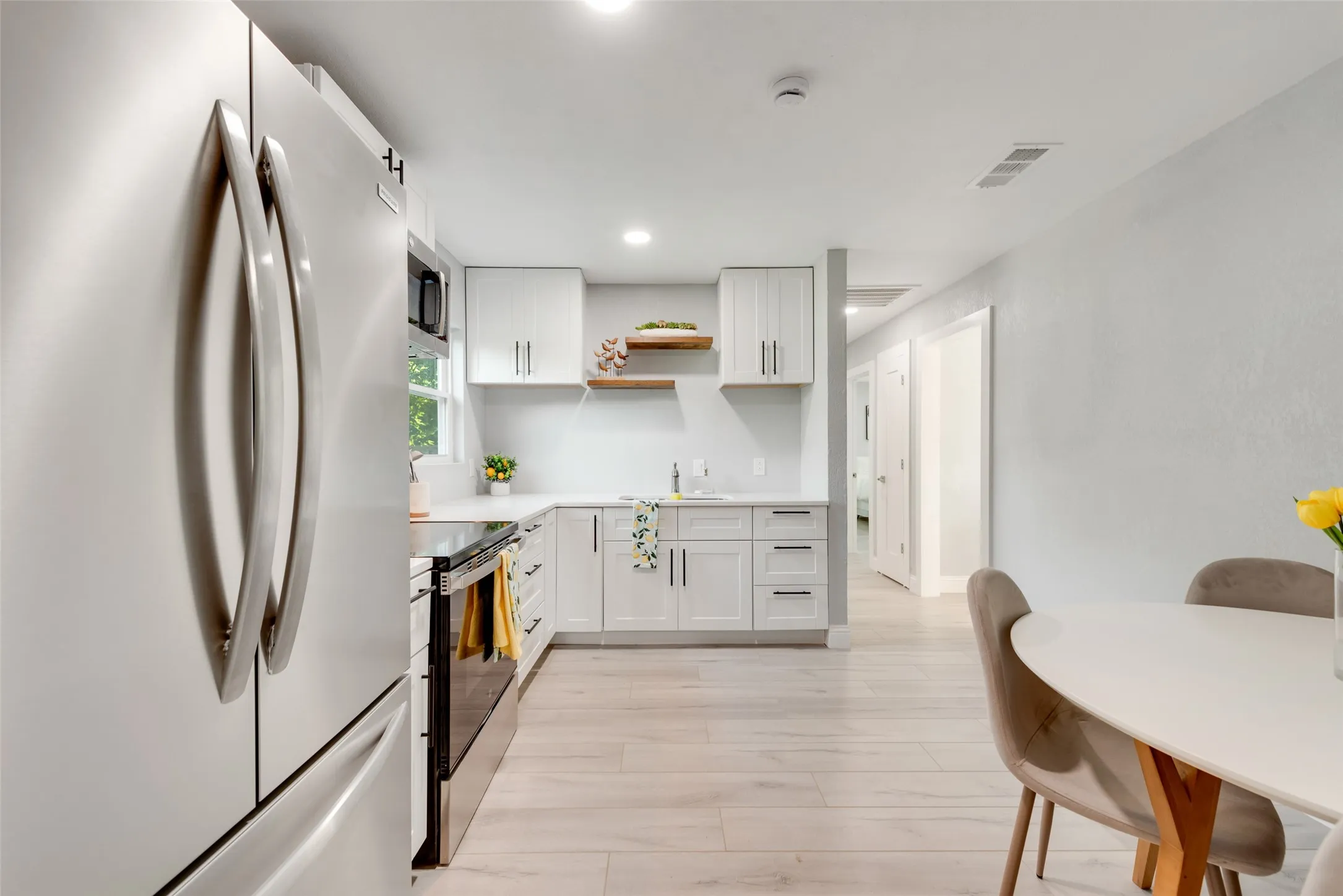 Modern kitchen featuring stainless steel appliances, white cabinetry, light-colored countertops, and wood-finish flooring