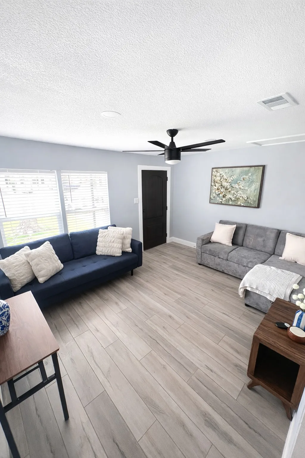 Spacious area with wood-finish flooring, multiple windows with blinds, a ceiling fan, and a solid black interior door