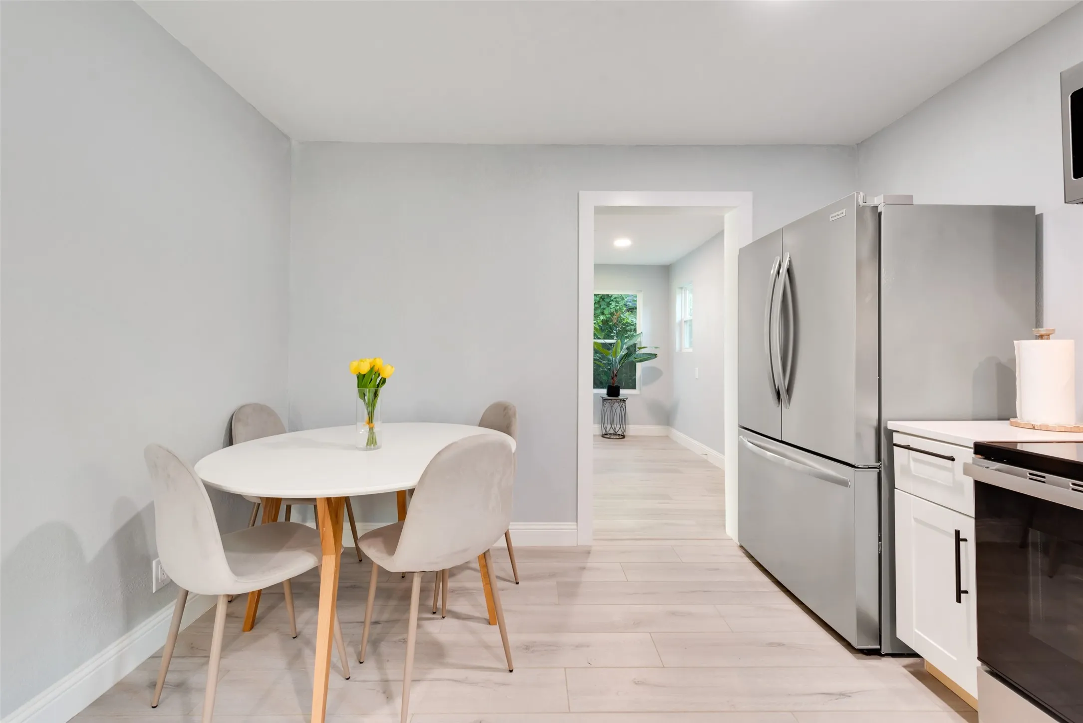 White cabinetry with black hardware, stainless steel refrigerator, white countertops, and wood-finish flooring