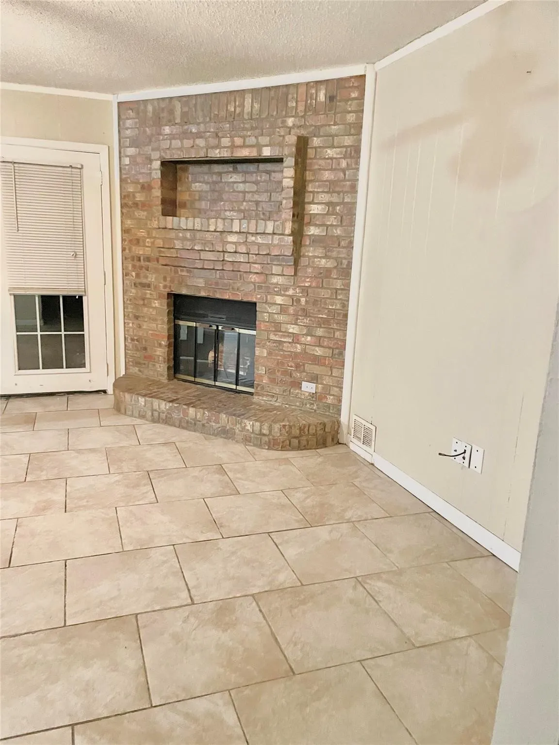 Unfurnished living room featuring crown molding, a textured ceiling, and a brick fireplace