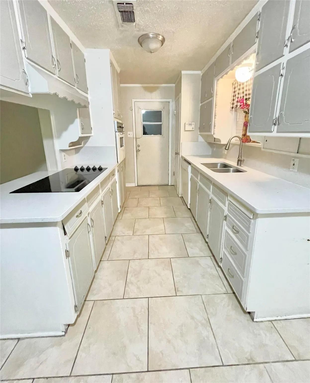 Kitchen featuring light tile patterned flooring, a textured ceiling, white appliances, and sink