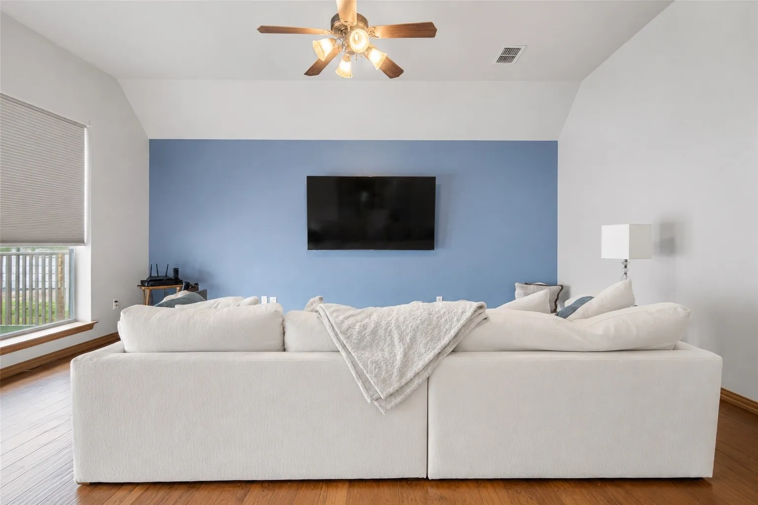Wood-finish flooring, vaulted ceiling, ceiling fan with integrated lighting, built-in window and window treatments, and mounted television