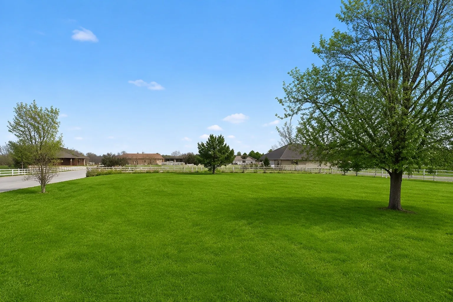 Expansive green lawn with mature trees and a white fence