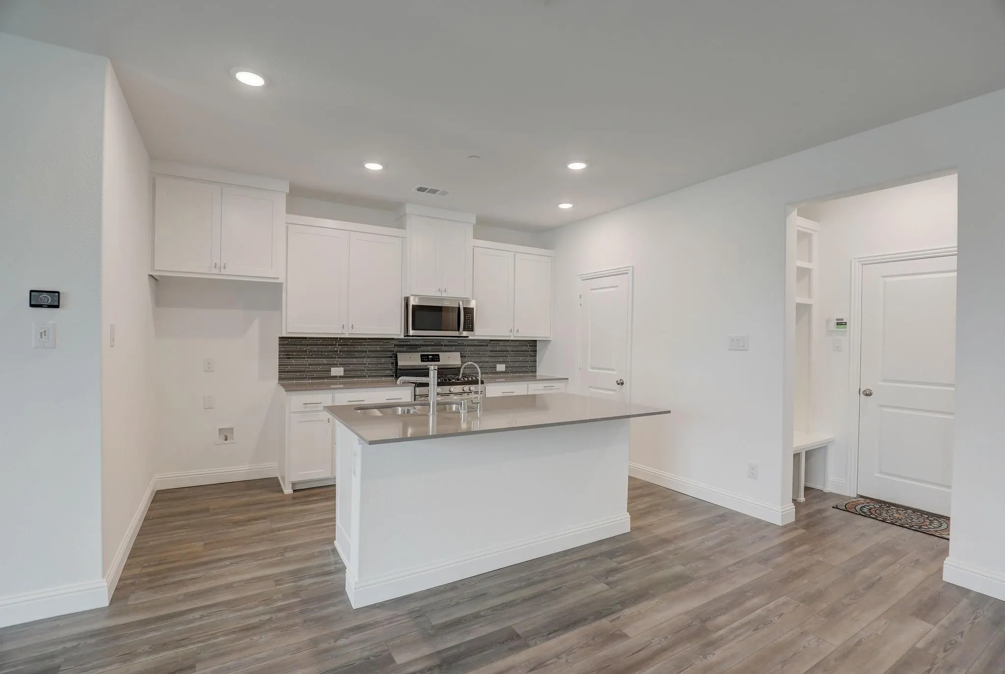 Contemporary kitchen featuring white cabinetry, a central island with a sink, stainless steel appliances, and wood-finish flooring