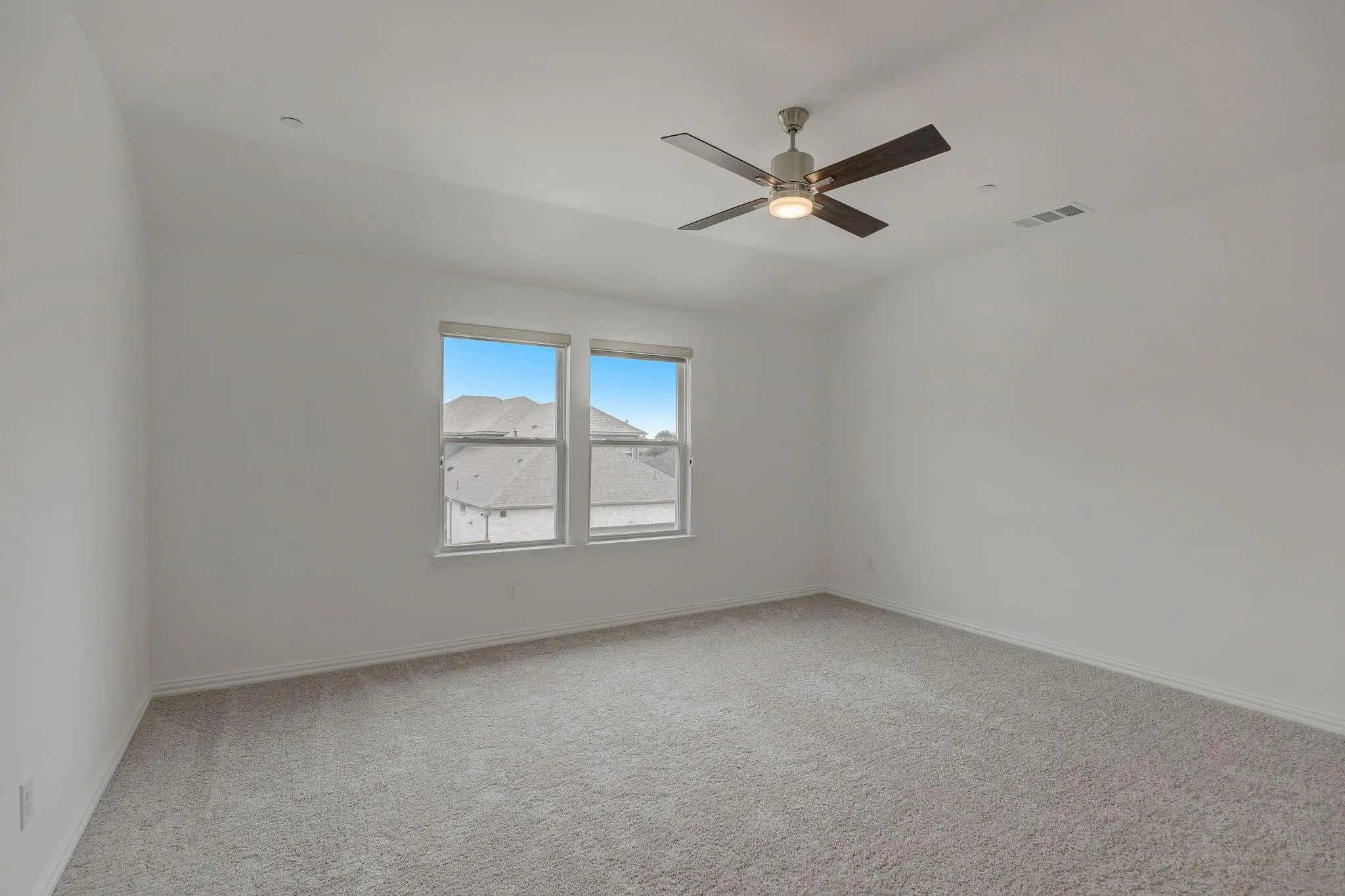 Spacious room featuring light gray carpeting, two windows with white frames, a ceiling fan with brushed nickel hardware and dark wood-finish blades, and recessed lighting
