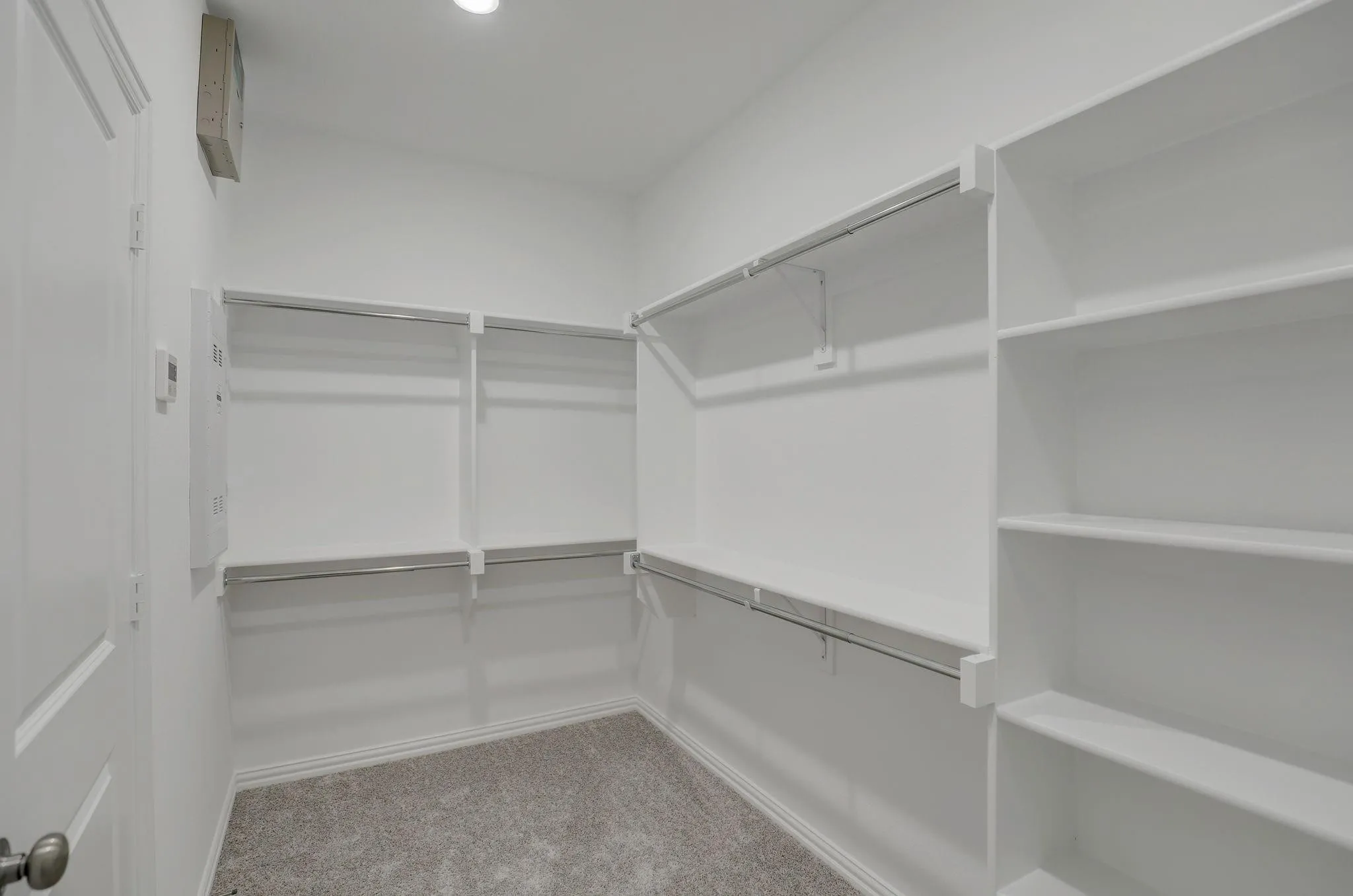 Built-in shelving, multiple hanging rods, recessed ceiling light, white painted walls, and carpet flooring
