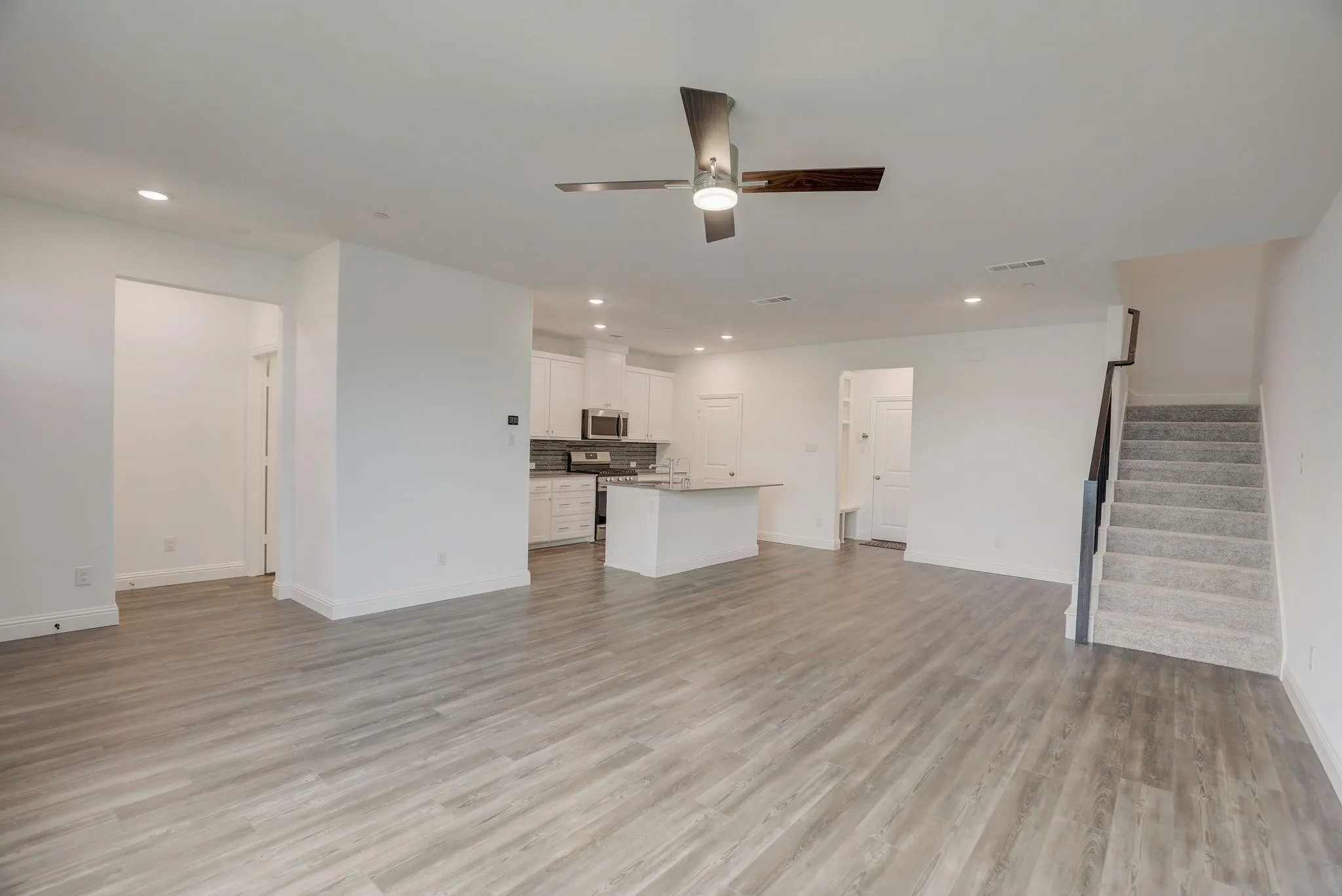 Spacious open-concept layout with wood-finish flooring, recessed lighting, and a contemporary ceiling fan
