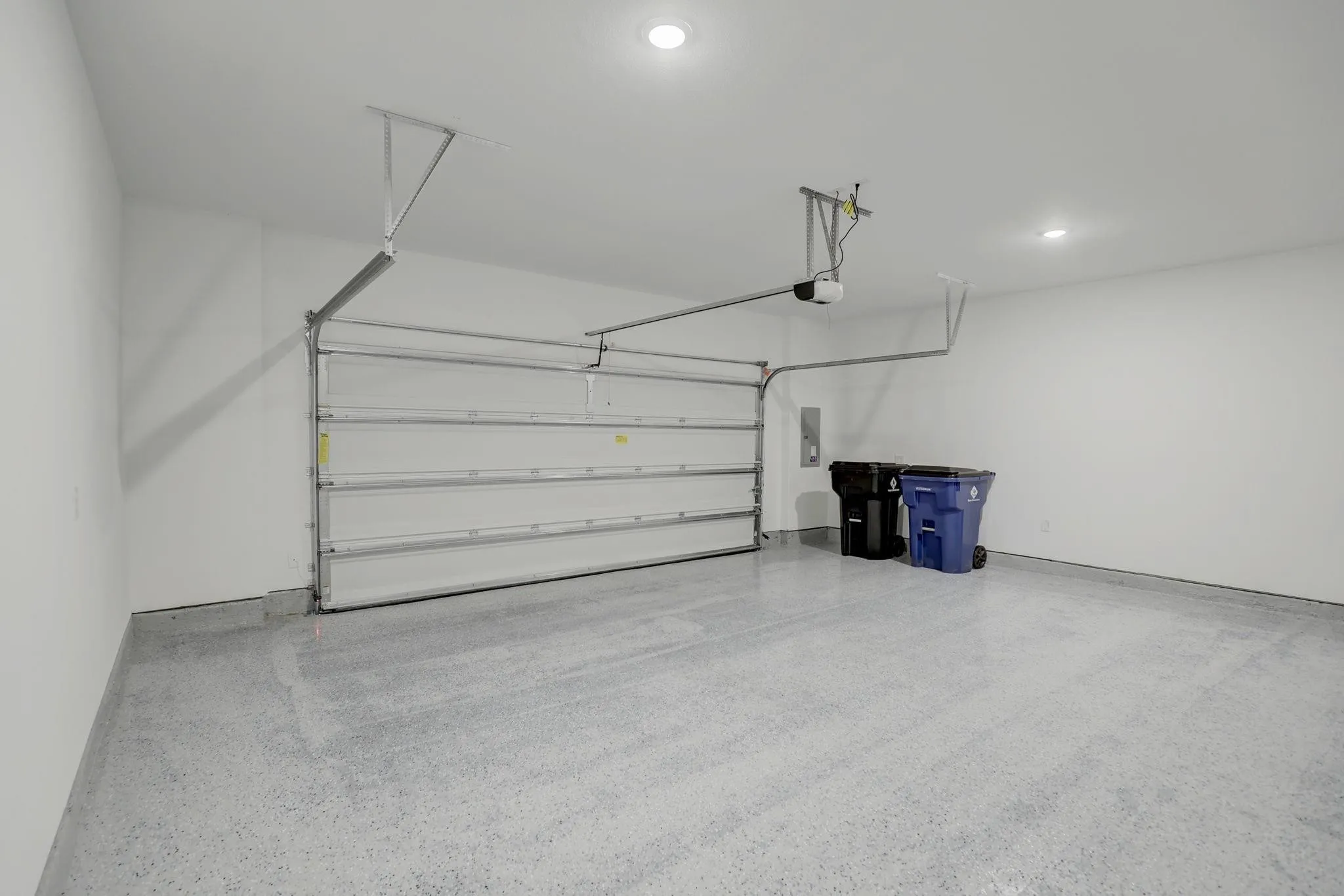 Attached garage featuring a sectional overhead door, motor-driven opener, recessed ceiling lighting, and a speckled epoxy floor finish