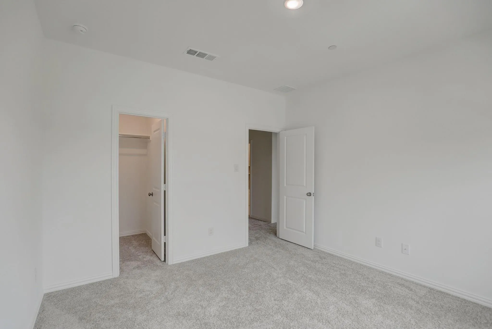 Spacious bedroom featuring neutral wall finishes, carpet flooring, and dual closet access with white panel doors