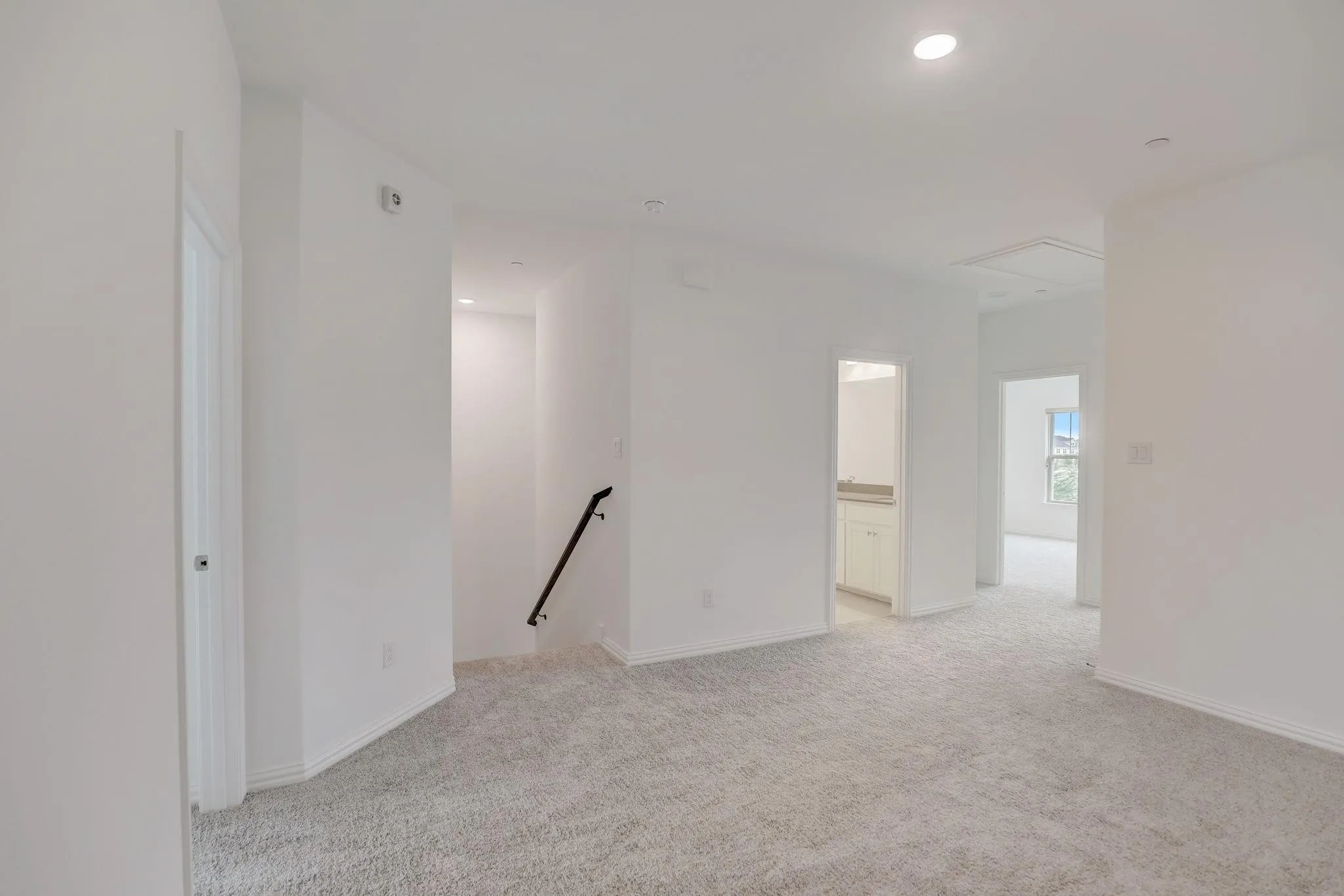 Carpeted hallway with white walls, recessed lighting, and a black handrail leading to a lower level