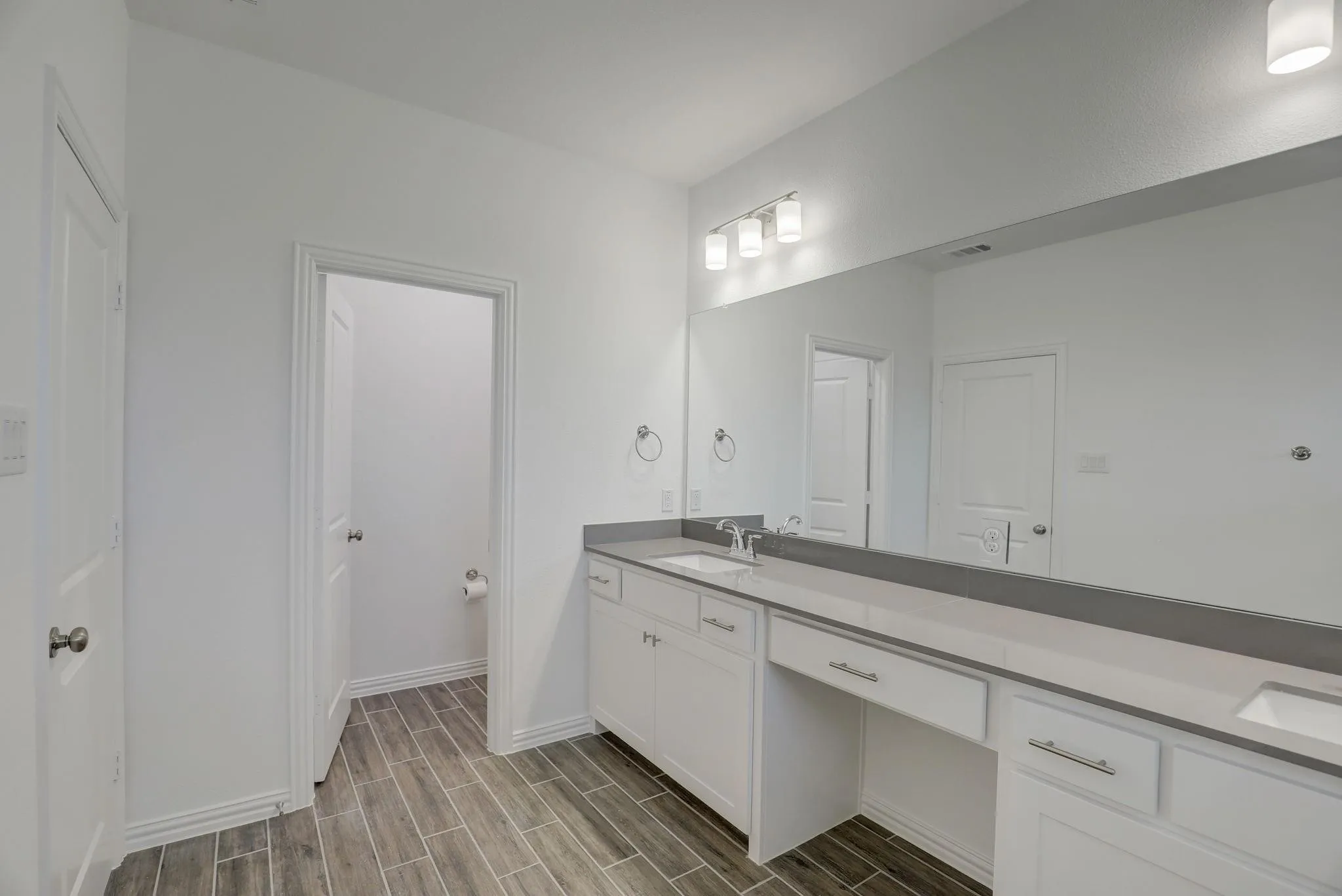 White shaker cabinetry with modern hardware, light gray countertop, undermount sinks, and plank-style tile flooring