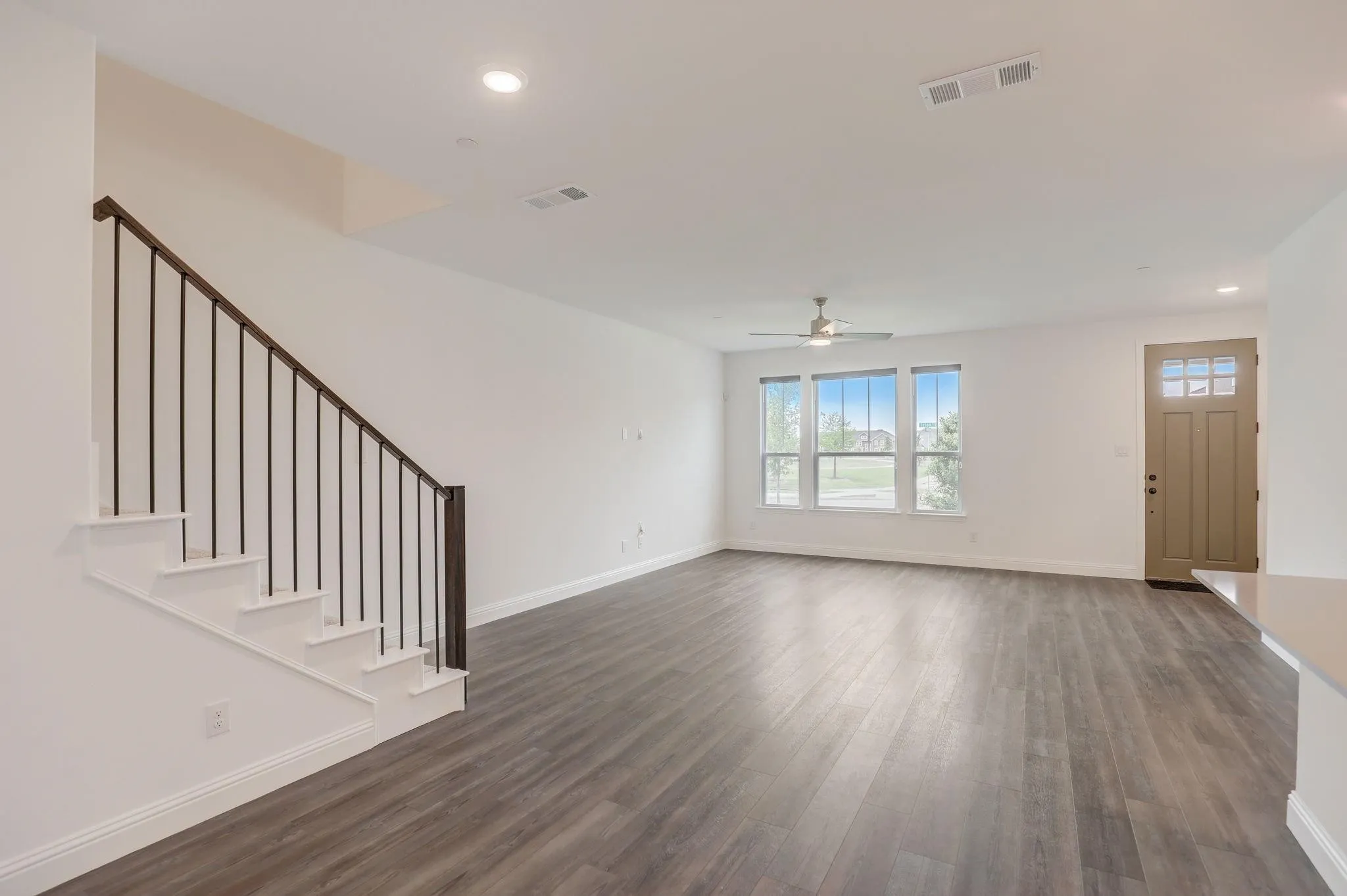Spacious living area featuring wood-finish flooring, ample natural light, a contemporary ceiling fan, and recessed lighting