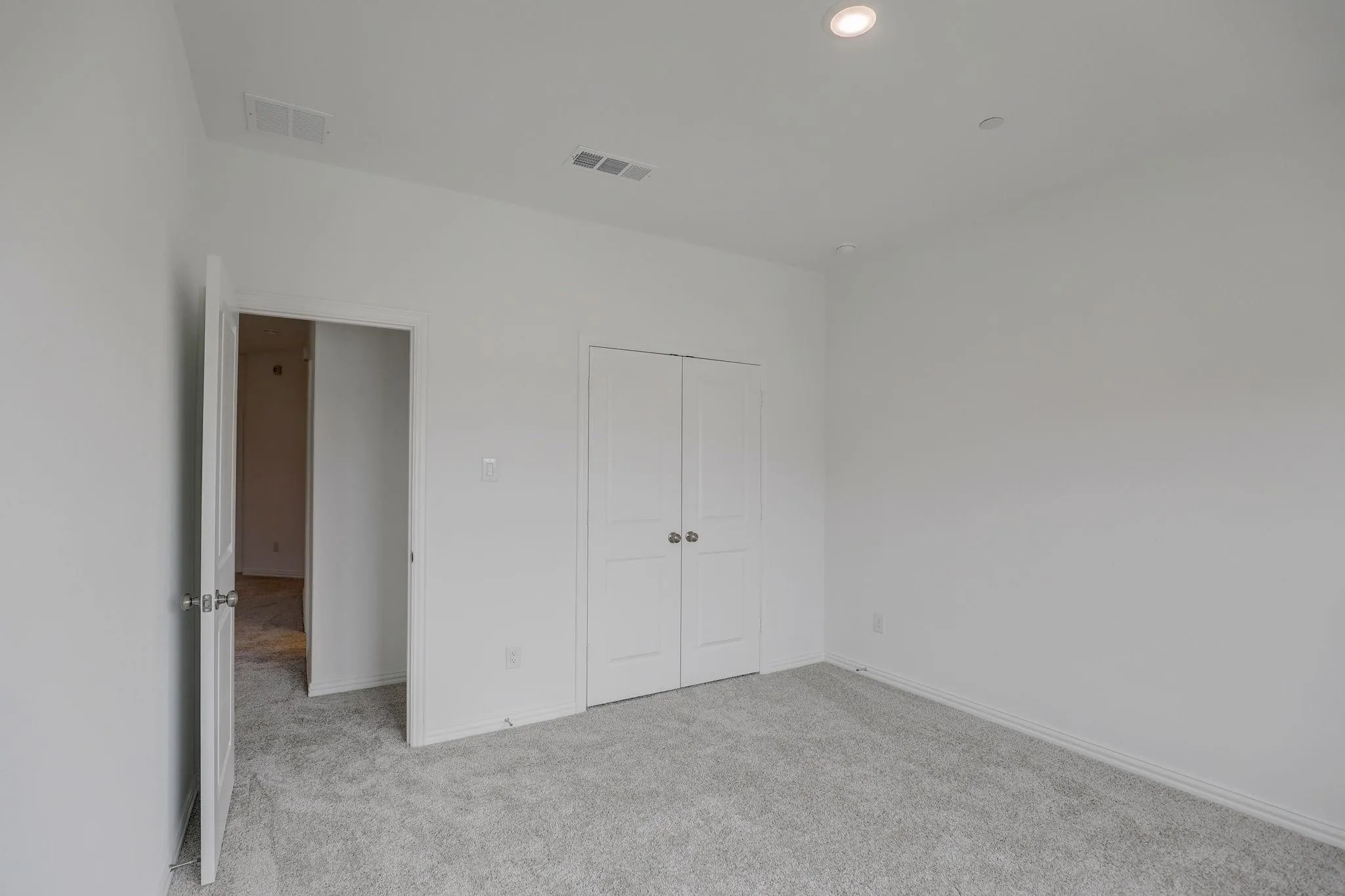 Recessed ceiling lighting, light gray wall-to-wall carpeting, white interior doors, and a double-door closet