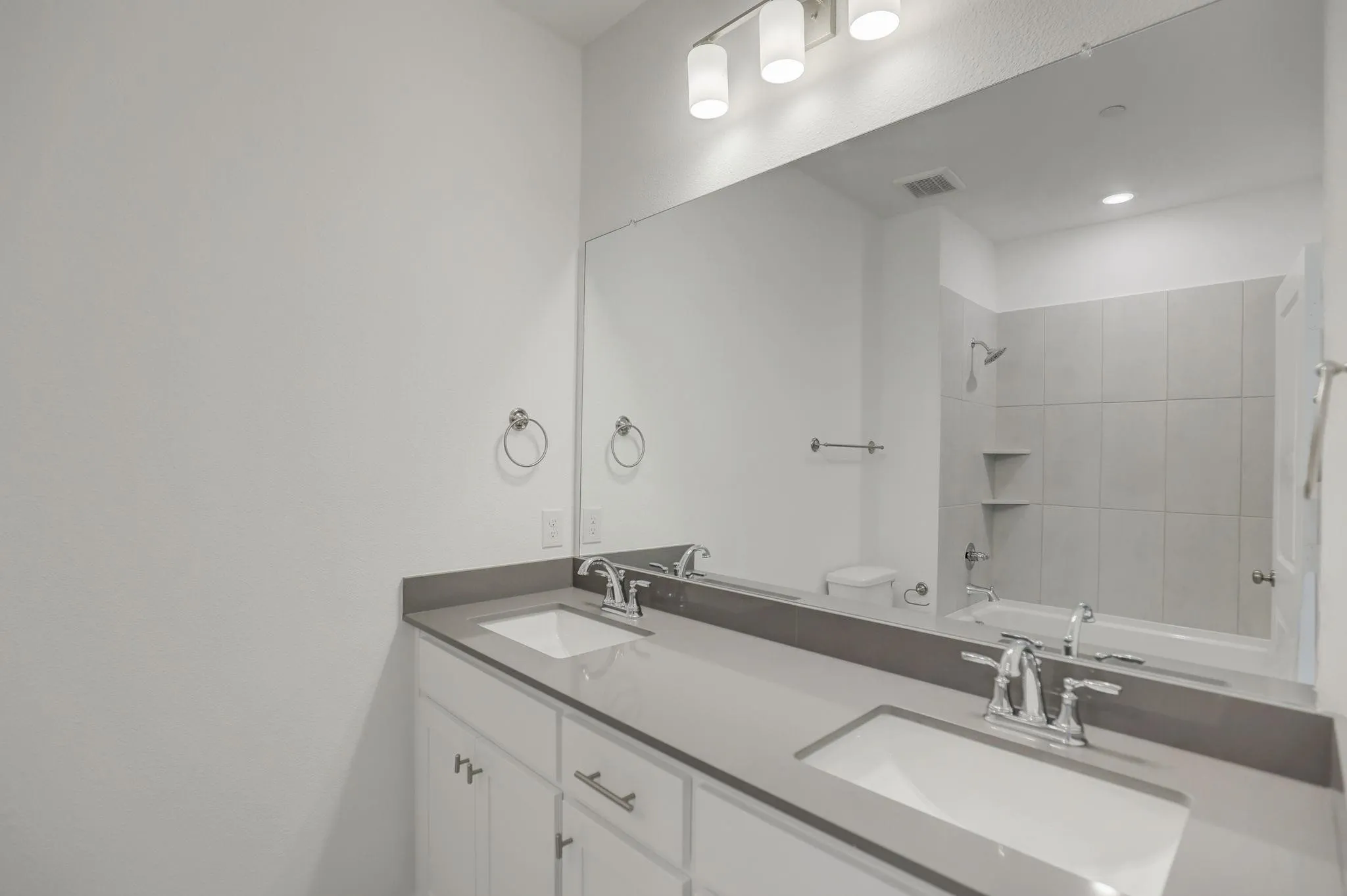 Dual undermount sinks with chrome fixtures, a broad vanity mirror, and white cabinetry